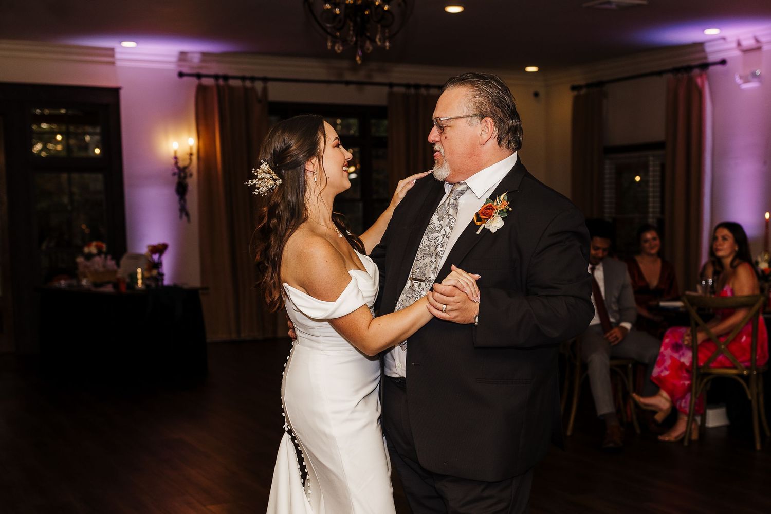 A couple shares a joyful dance moment together at an elegant reception venue with purple lighting.