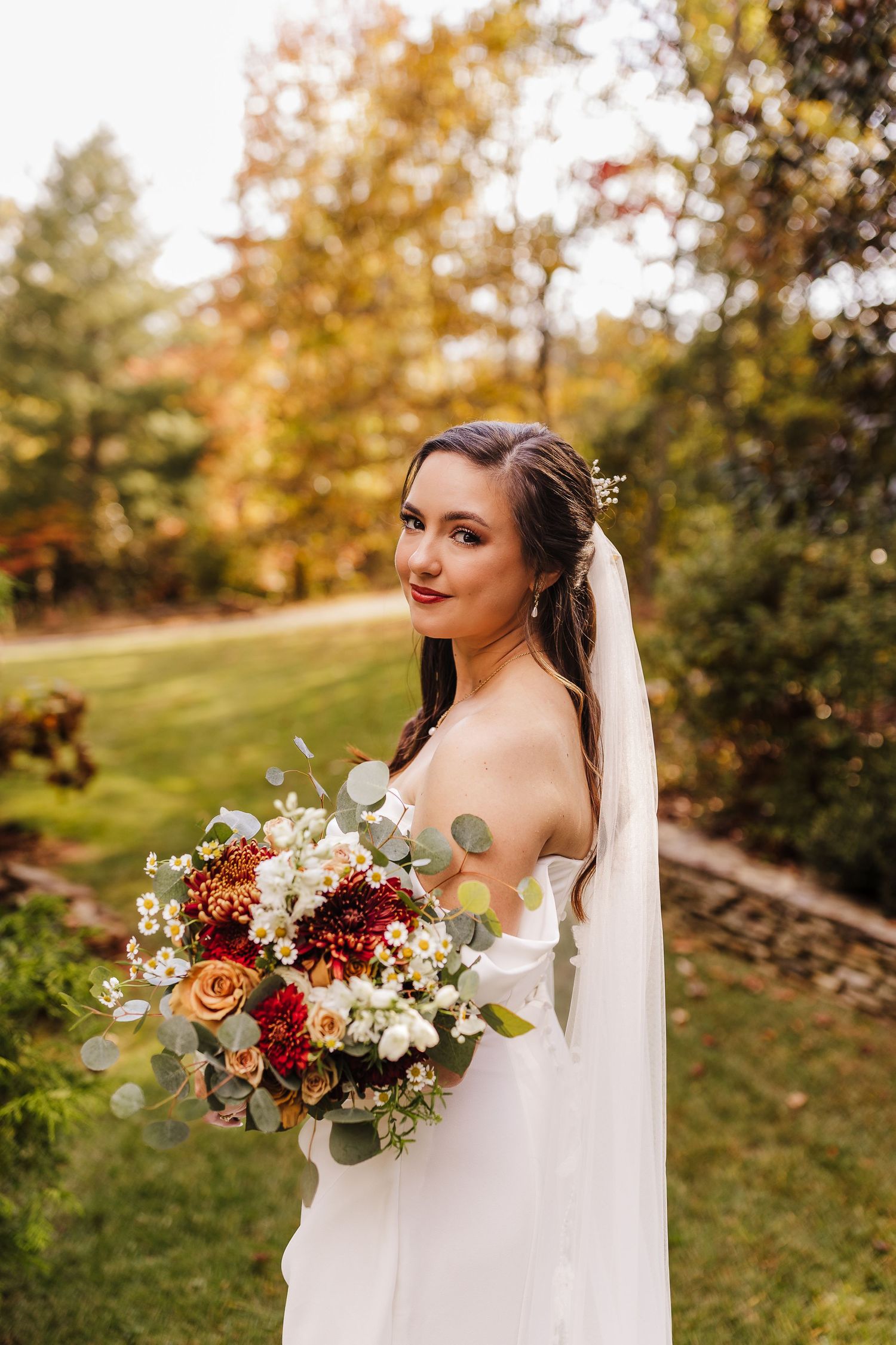 Bride holding a stunning autumn bouquet with red and white flowers against a fall landscape backdrop.