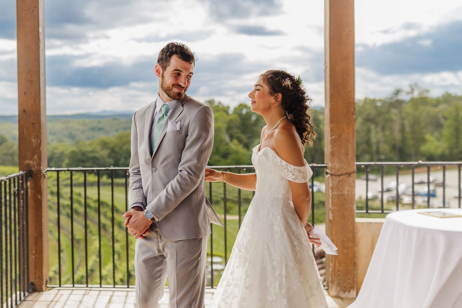 Bride and groom share a tender first look moment on a rustic outdoor balcony with scenic countryside views.