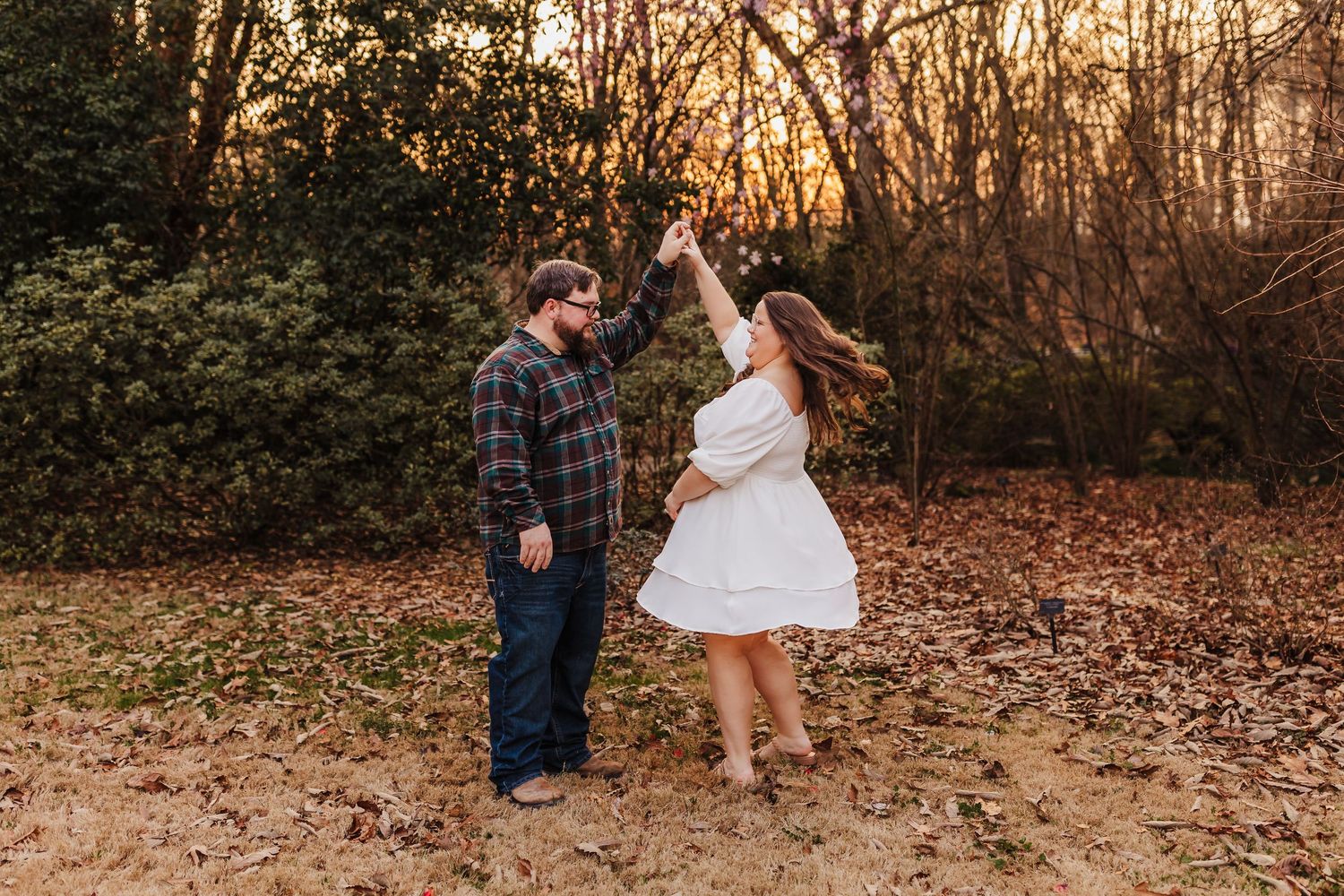 Playful couple dancing and twirling in autumn forest clearing at sunset.