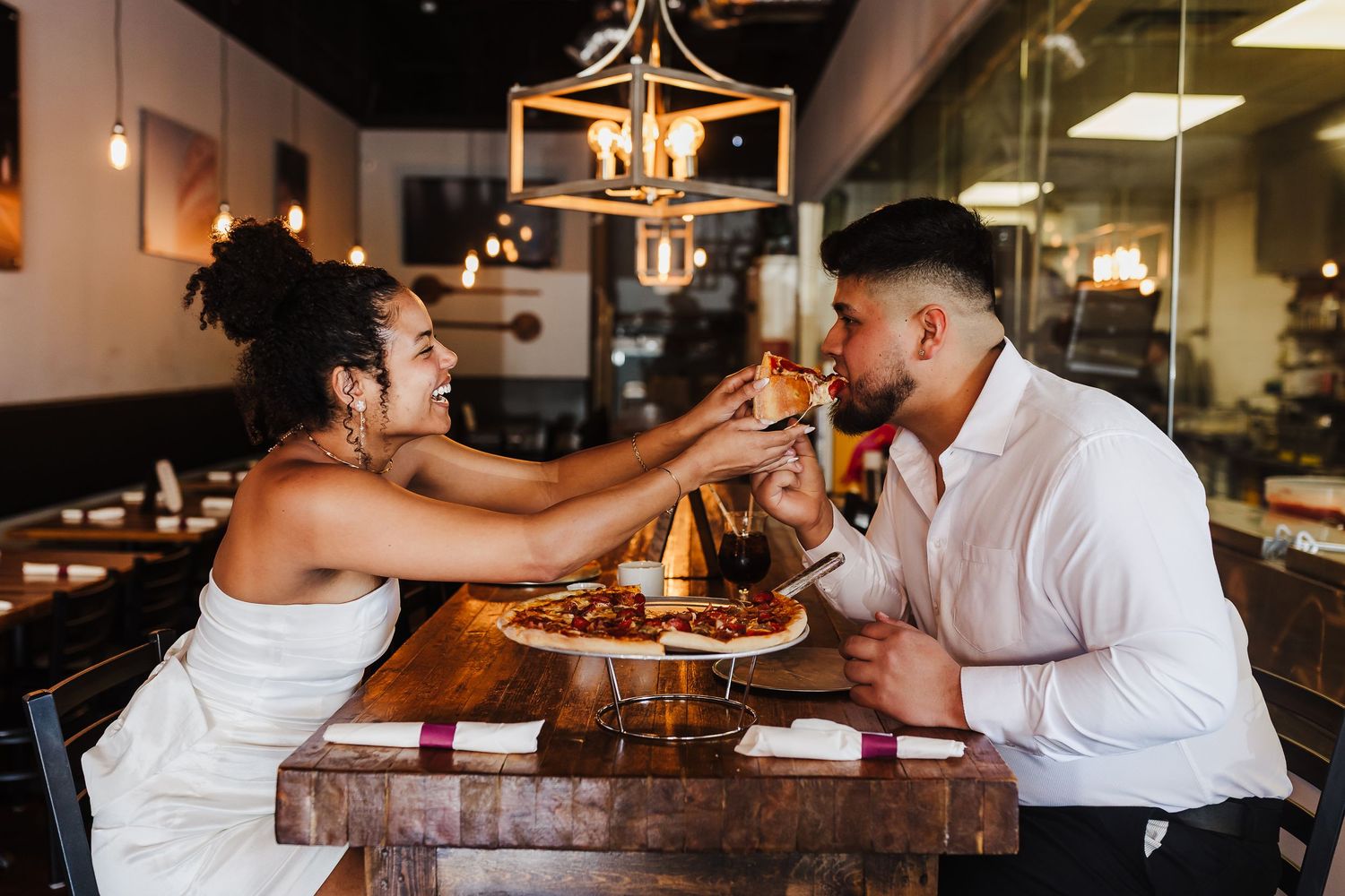 Engaged couple sharing pizza and laughing together during a fun engagement session at Vinny’s Little Italy.