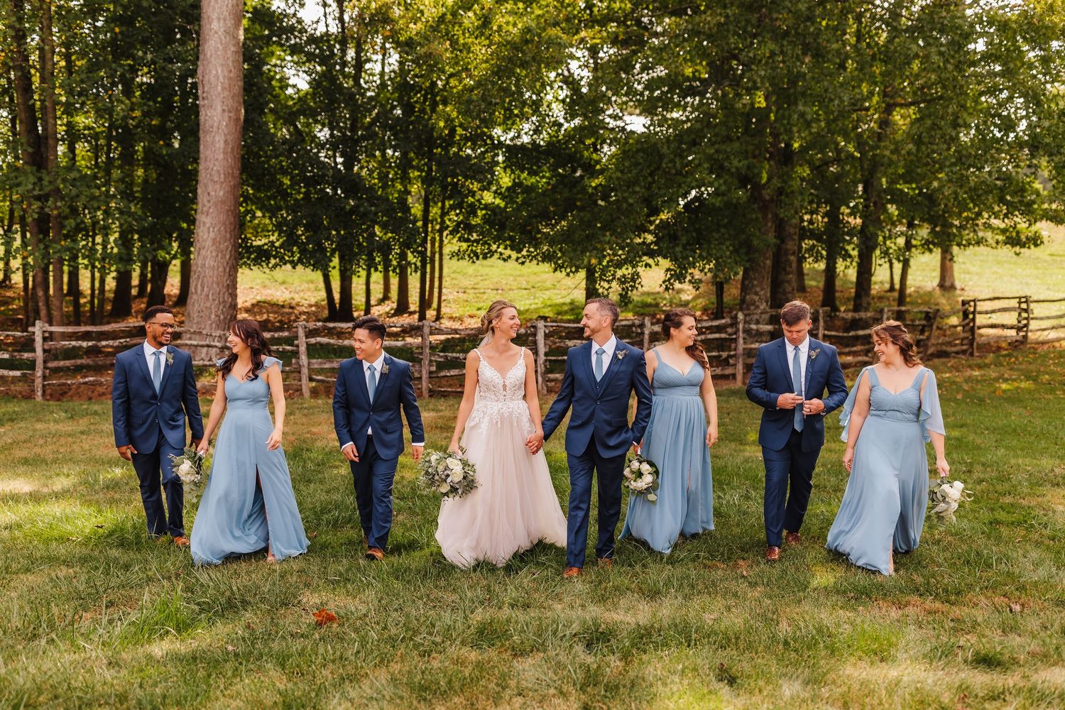 Wedding party poses together on grassy field with bridesmaids in light blue dresses.