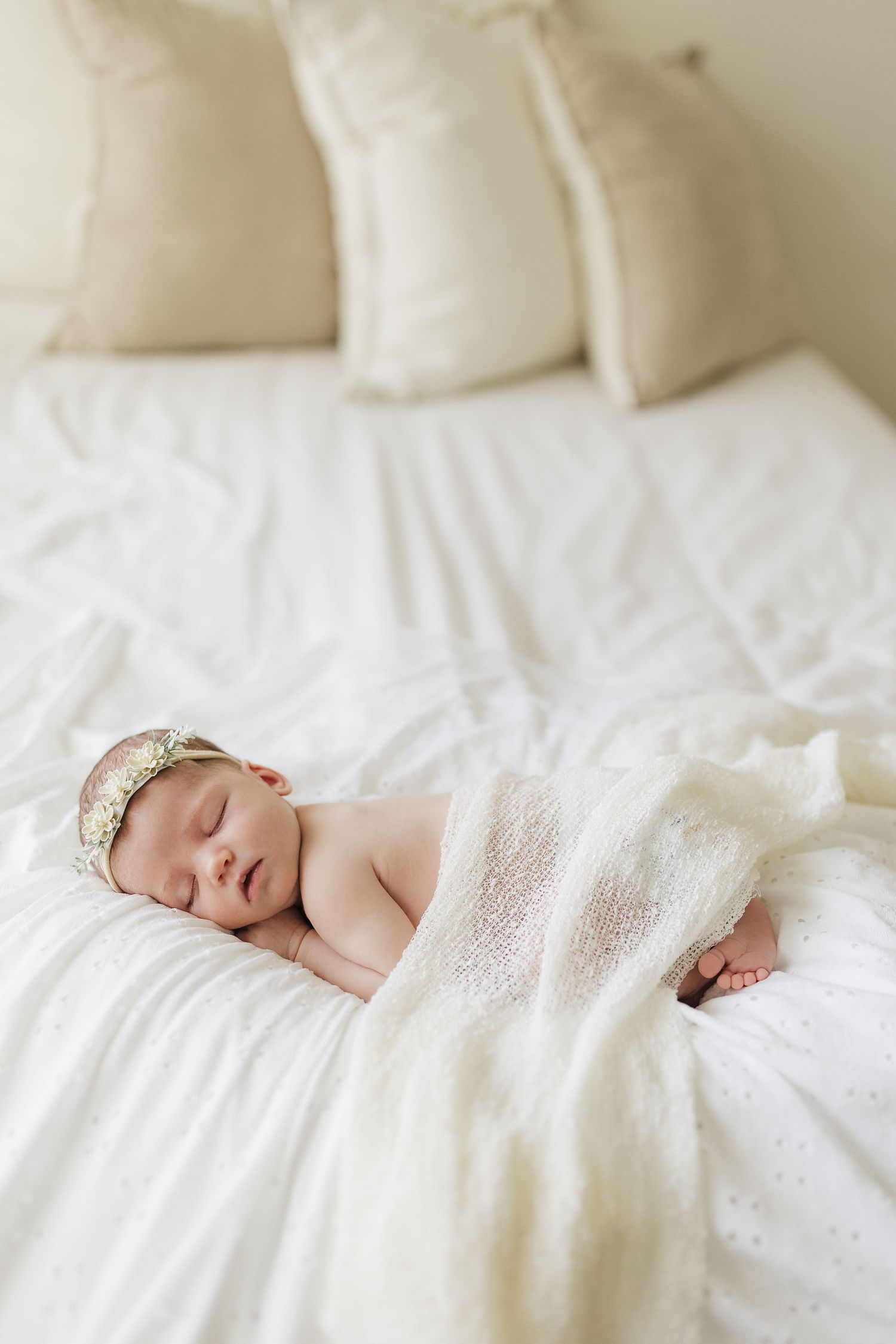 A sleeping baby wrapped in soft white blankets lies peacefully on crisp white bedding.
