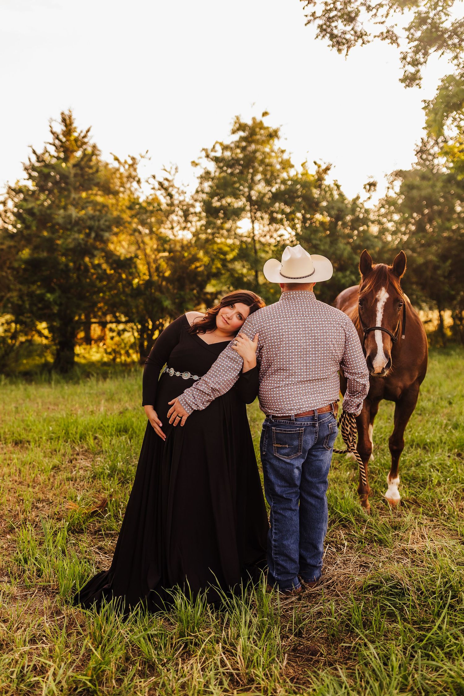 Maternity portrait of an expecting couple posing with a horse in a rustic field setting
