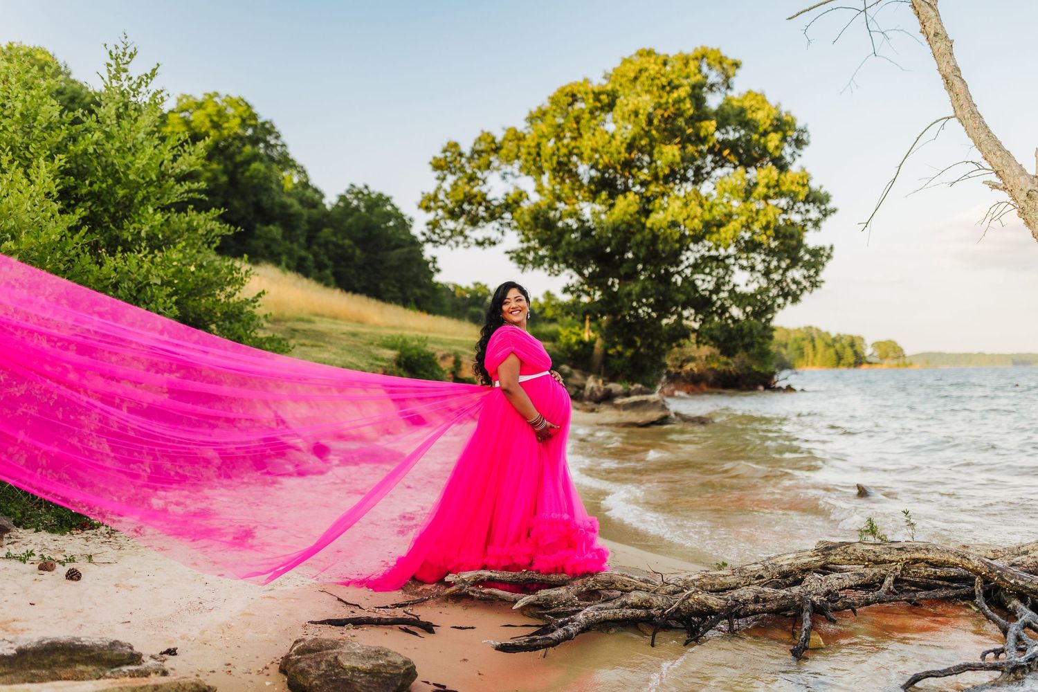 Maternity portrait at Lake Lanier featuring an expecting mother in a flowing pink dress caught in the wind.