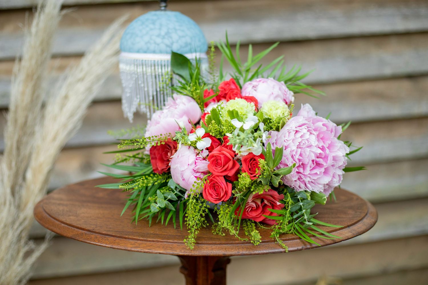 Vibrant pink and red flower bouquet with peonies and greenery arranged on a wooden table.