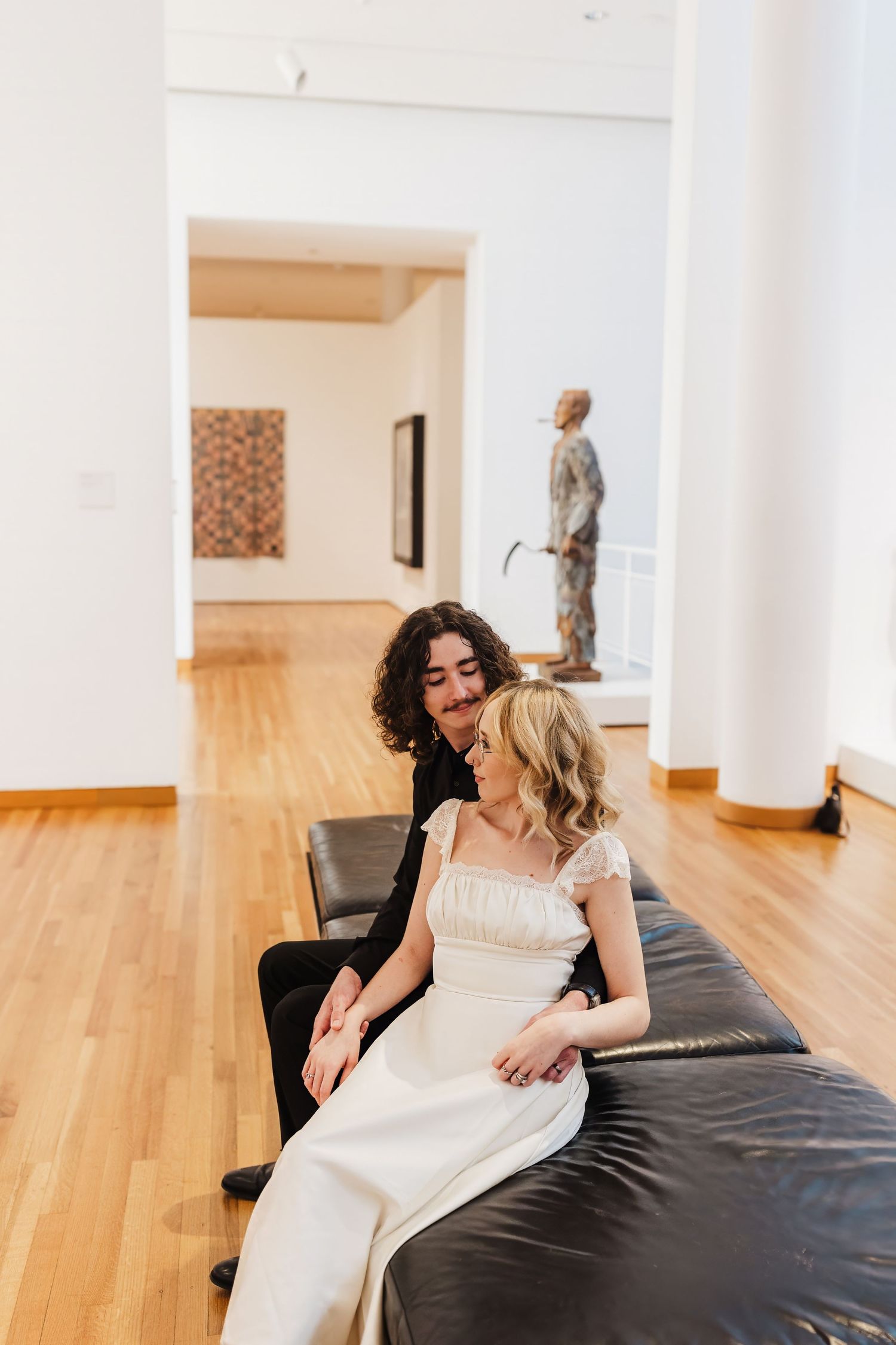 Two people relaxing on a black leather bench in a modern art gallery.