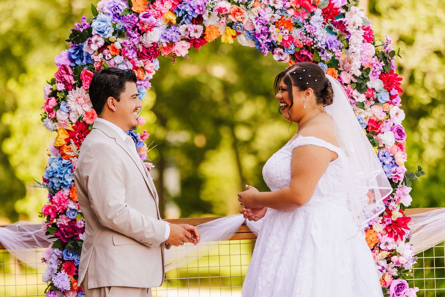 Wedding ceremony under vibrant floral arch with pink and purple blooms in outdoor garden setting.