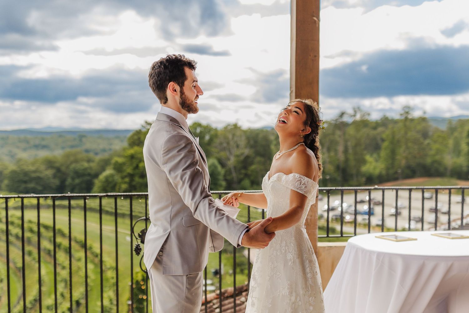 A joyful couple shares their first dance on a balcony overlooking lush green hills on their wedding day.