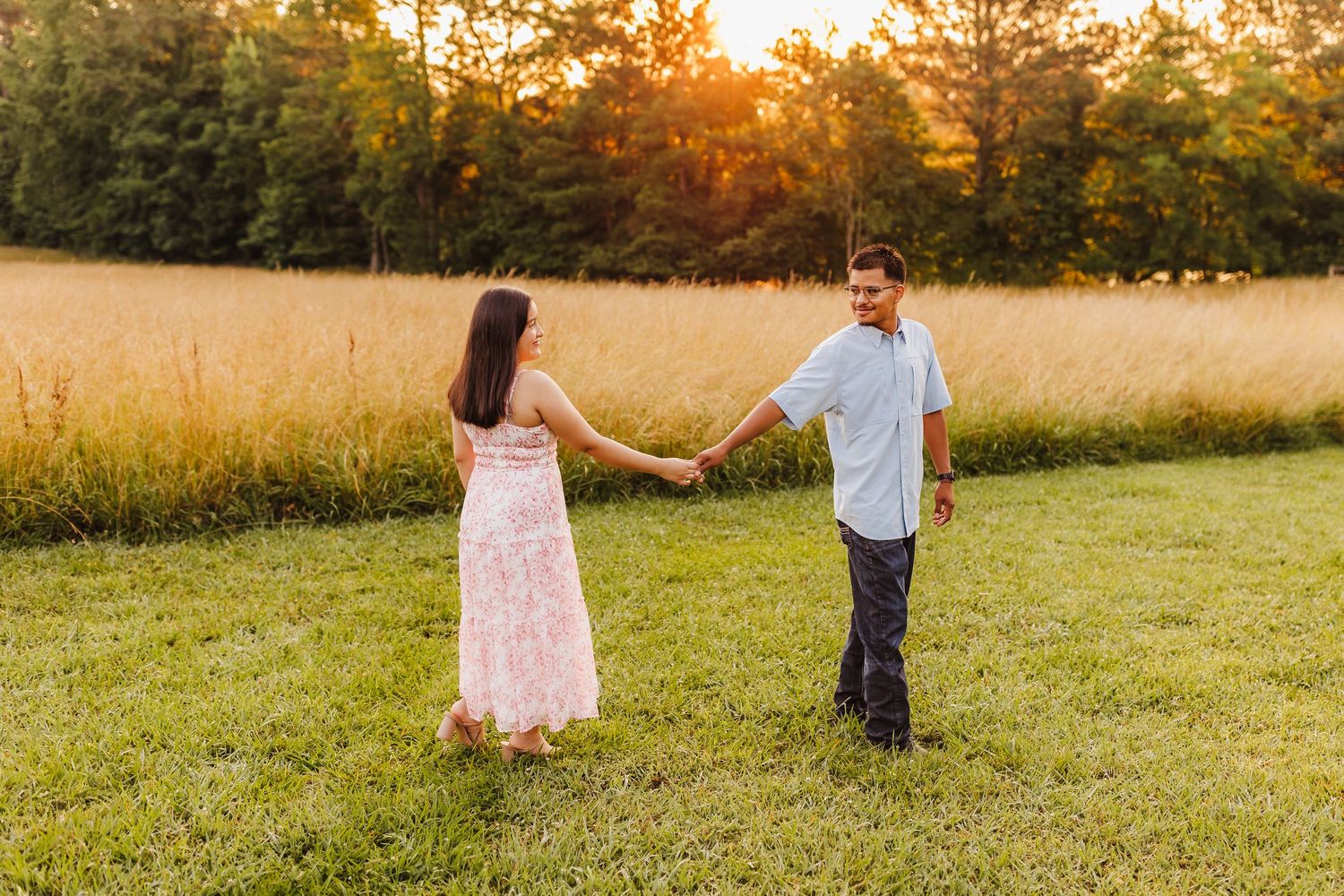 Couple holding hands in a golden field during sunset.
