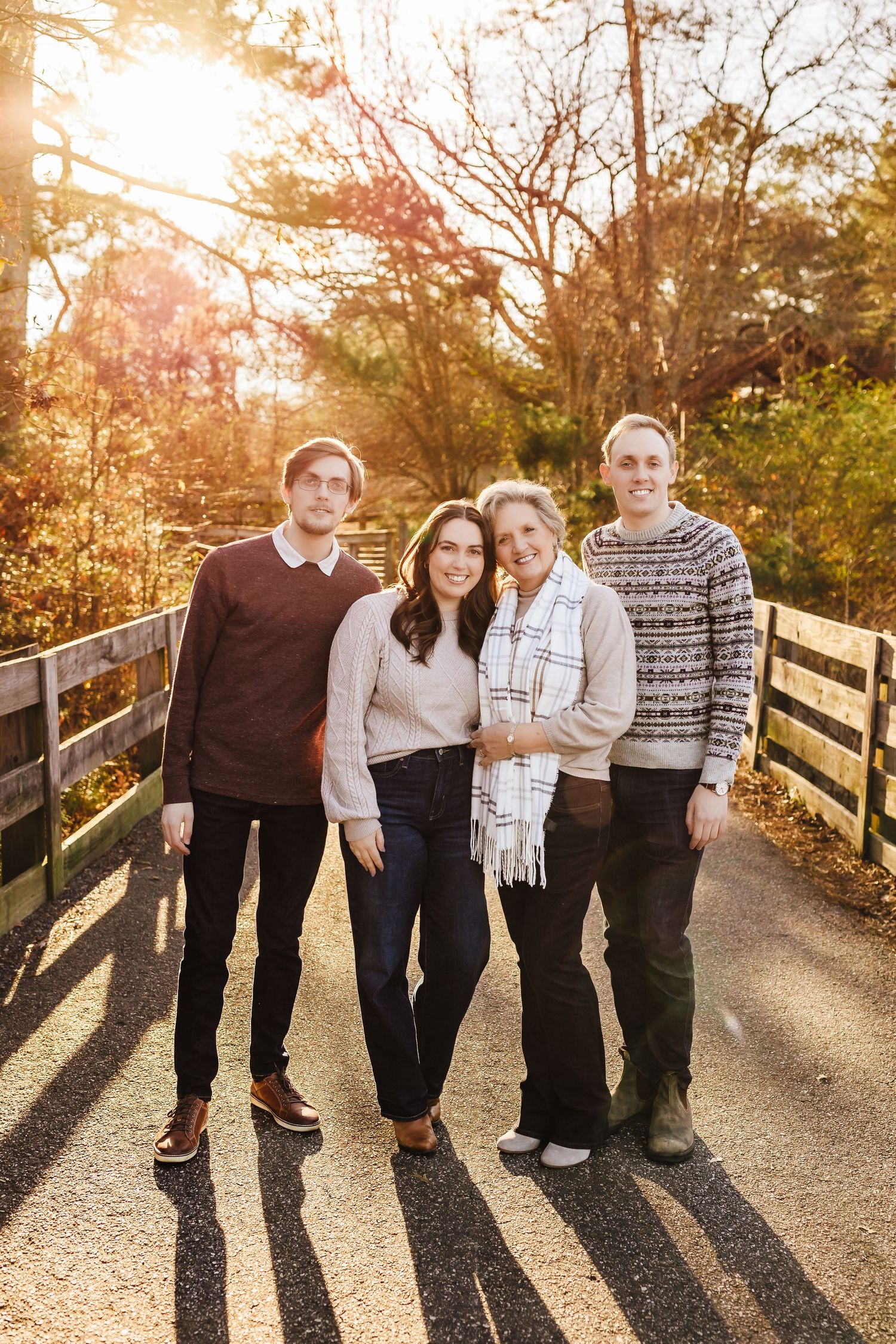 A family in coordinated neutral outfits poses together on a wooden bridge path during golden hour sunset.