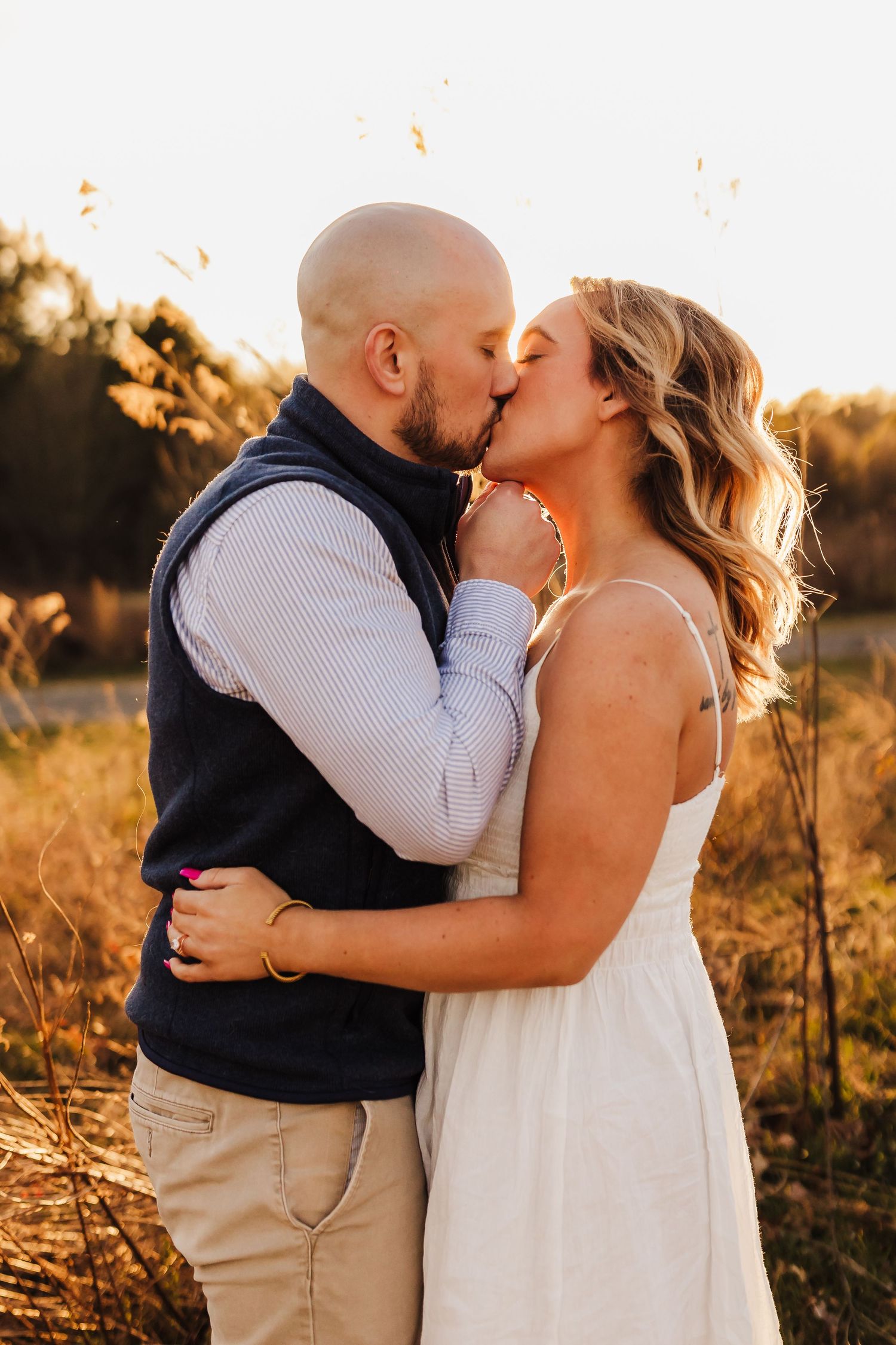 Romantic couple sharing tender kiss in golden sunlit field at sunset.
