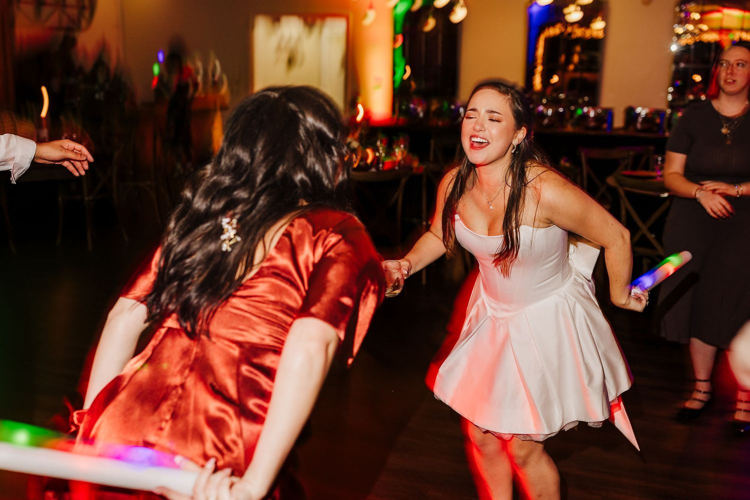 Wedding reception dance party with colorful lighting and energetic guests on the dance floor.