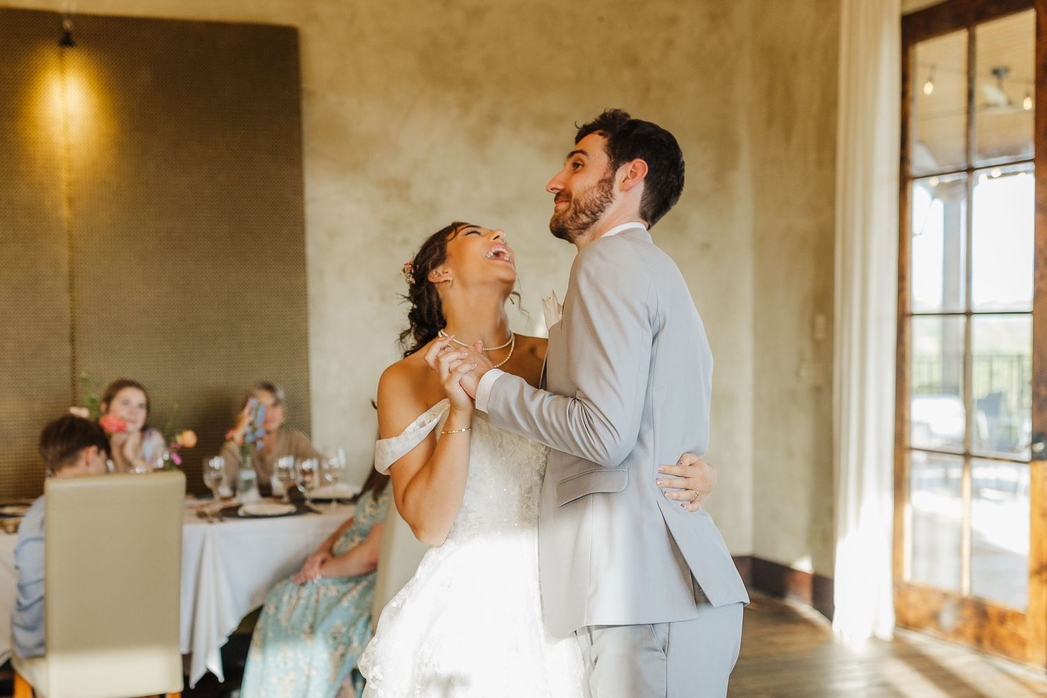 Bride and groom share their first dance, smiling joyfully, in an elegant wedding reception venue.