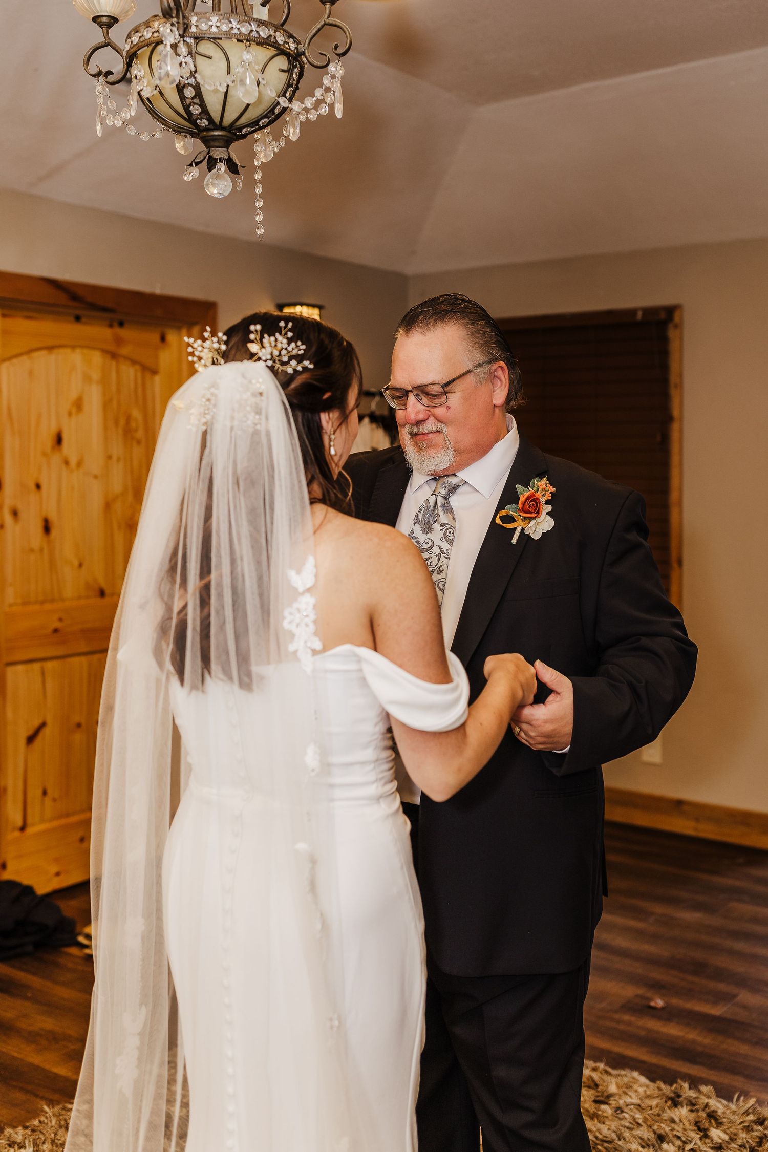 A touching first dance moment between newlyweds in an elegant indoor venue with wooden accents and chandeliers.