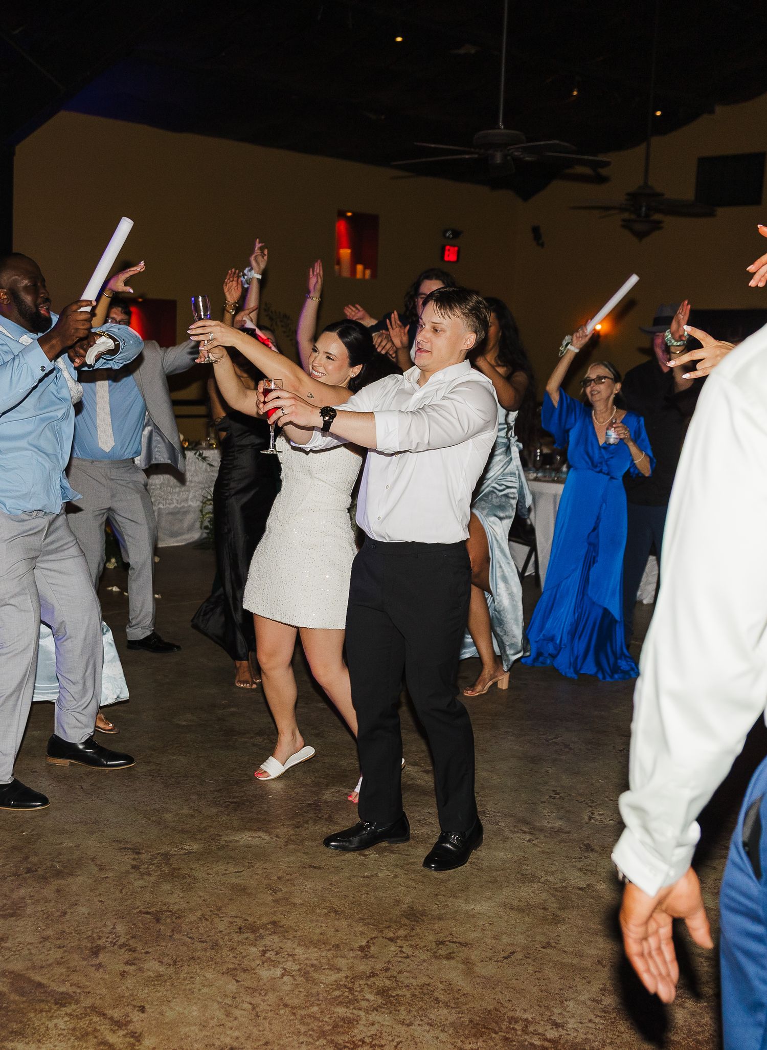 Guests dancing and celebrating at a lively wedding reception, holding glow sticks on a dance floor.