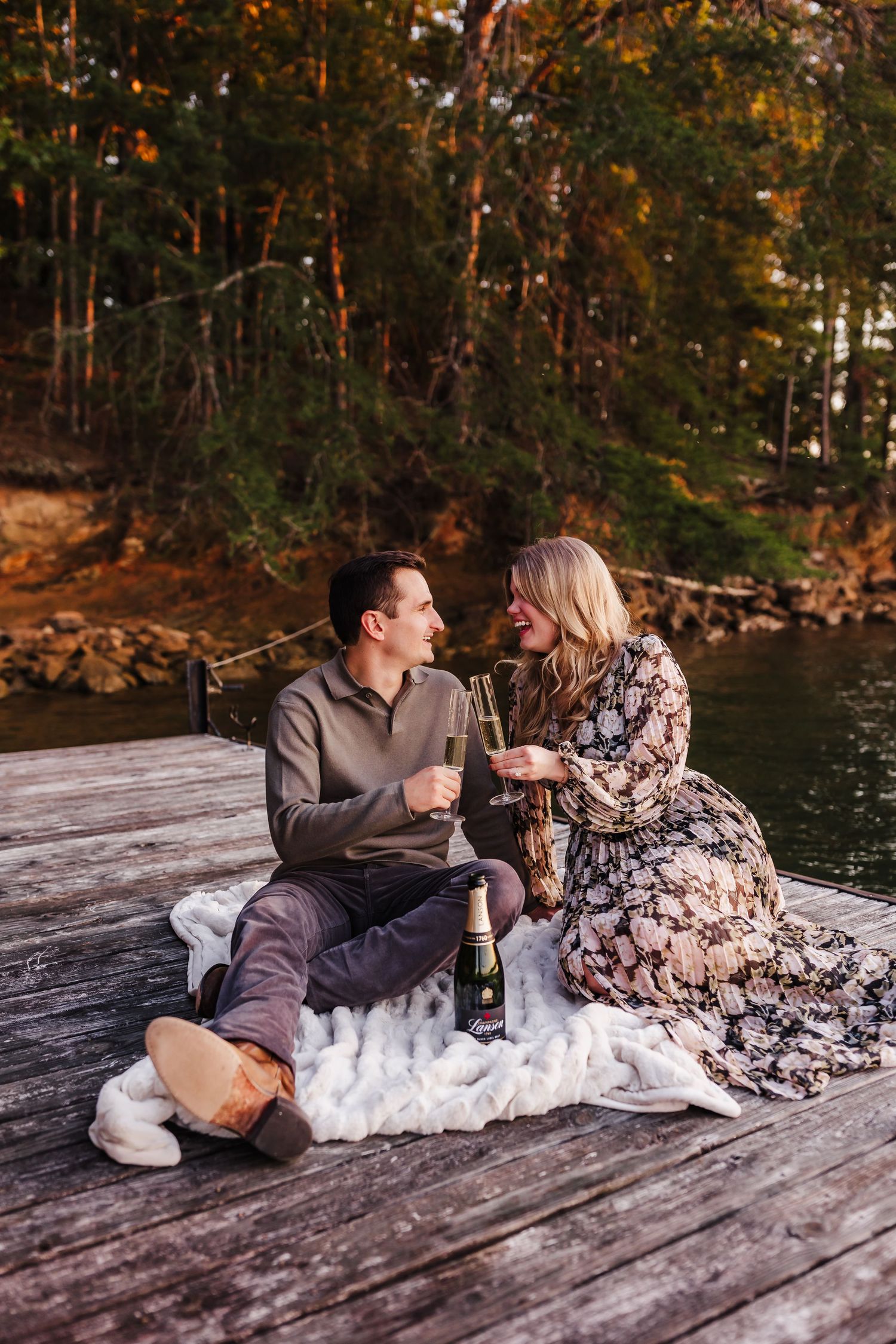 Couple enjoying wine together on a dock by a lake during autumn.
