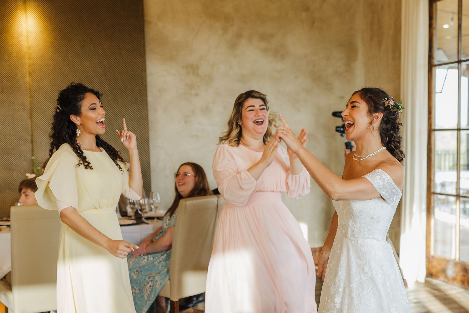 Bride and bridesmaids laughing and dancing together in elegant dresses during a joyful wedding celebration.