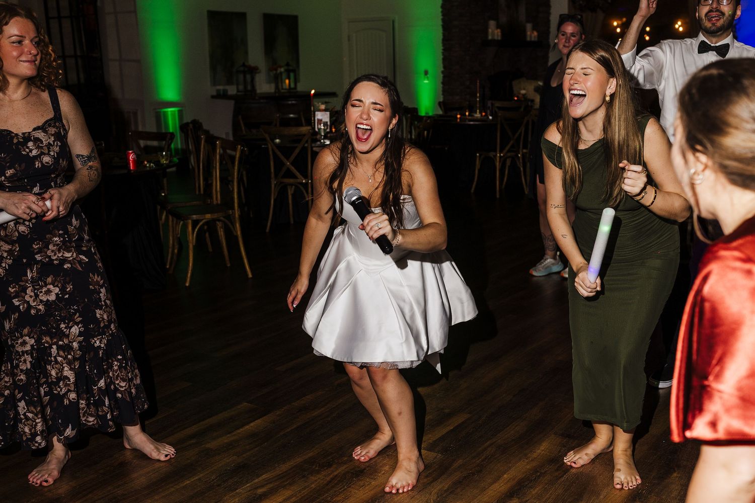 People dance and celebrate together on a dark dance floor illuminated by green lighting.