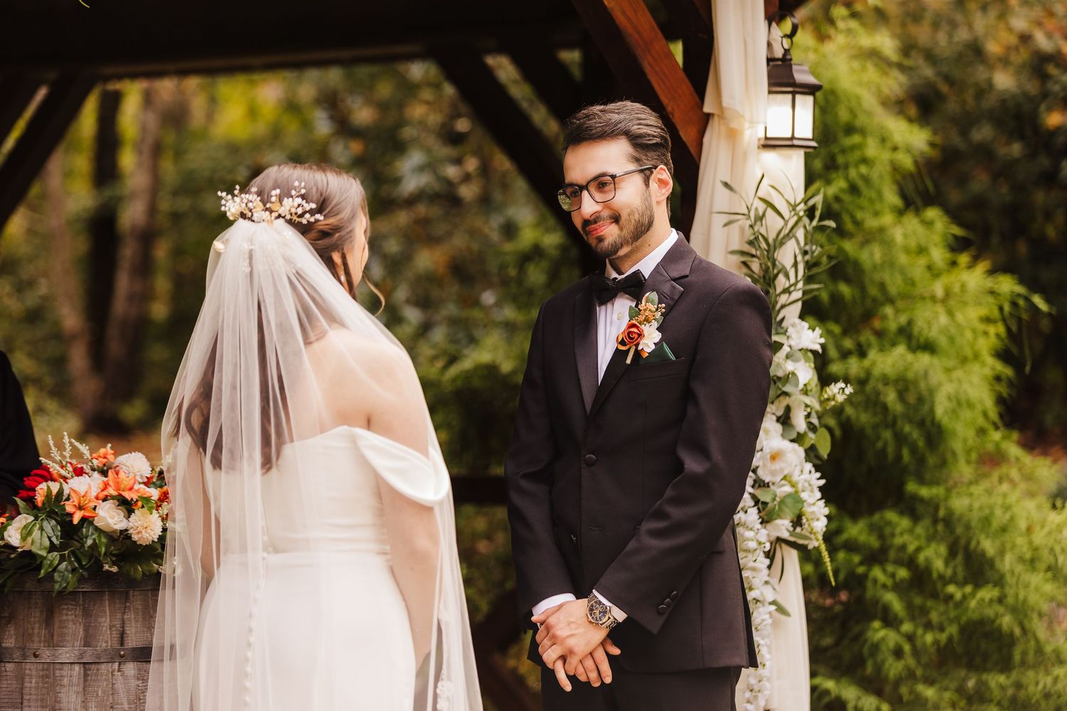 An outdoor wedding ceremony moment under a wooden pergola with greenery and floral decorations.