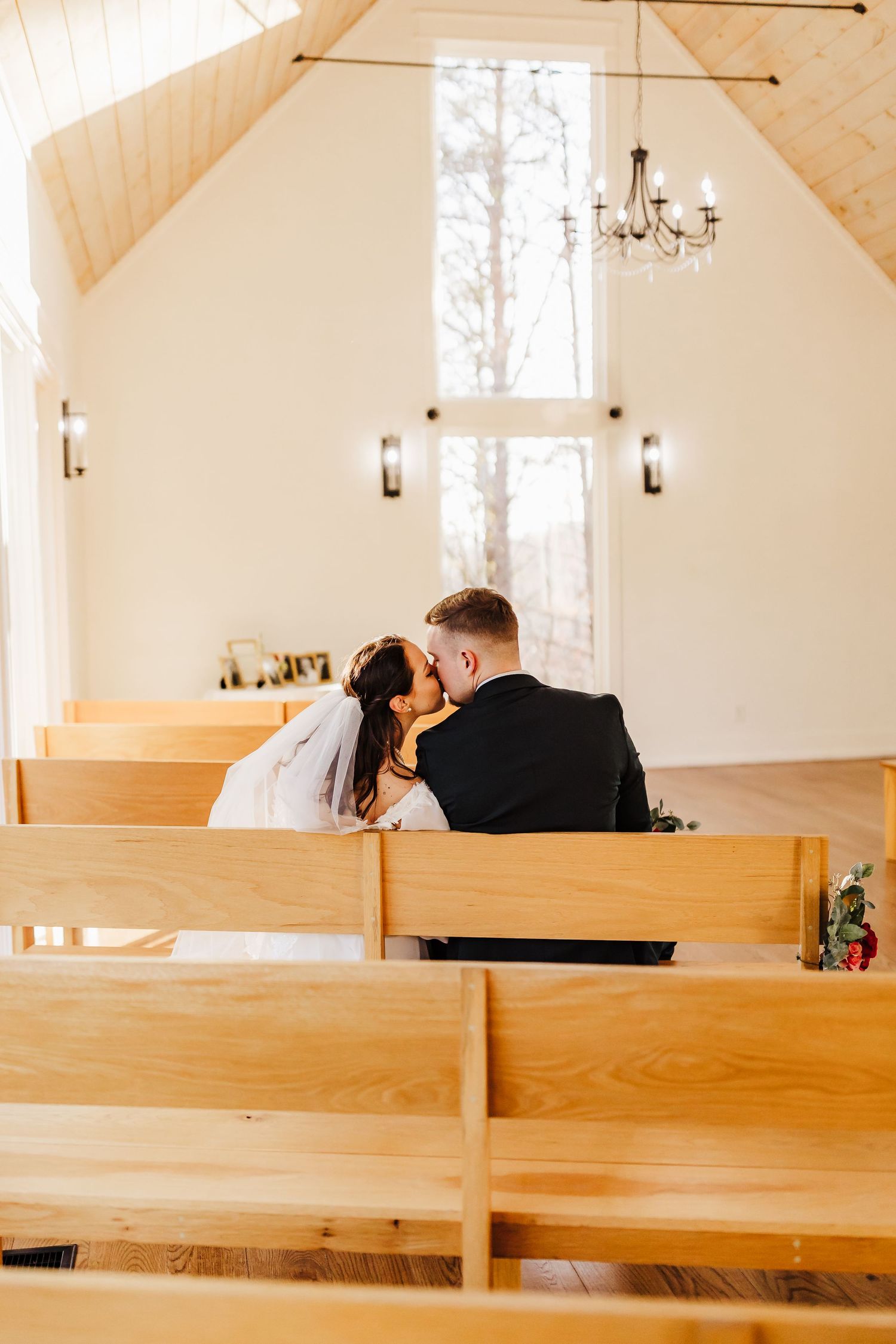 Couple sharing an intimate moment in a rustic chapel with wooden pews and a chandelier.
