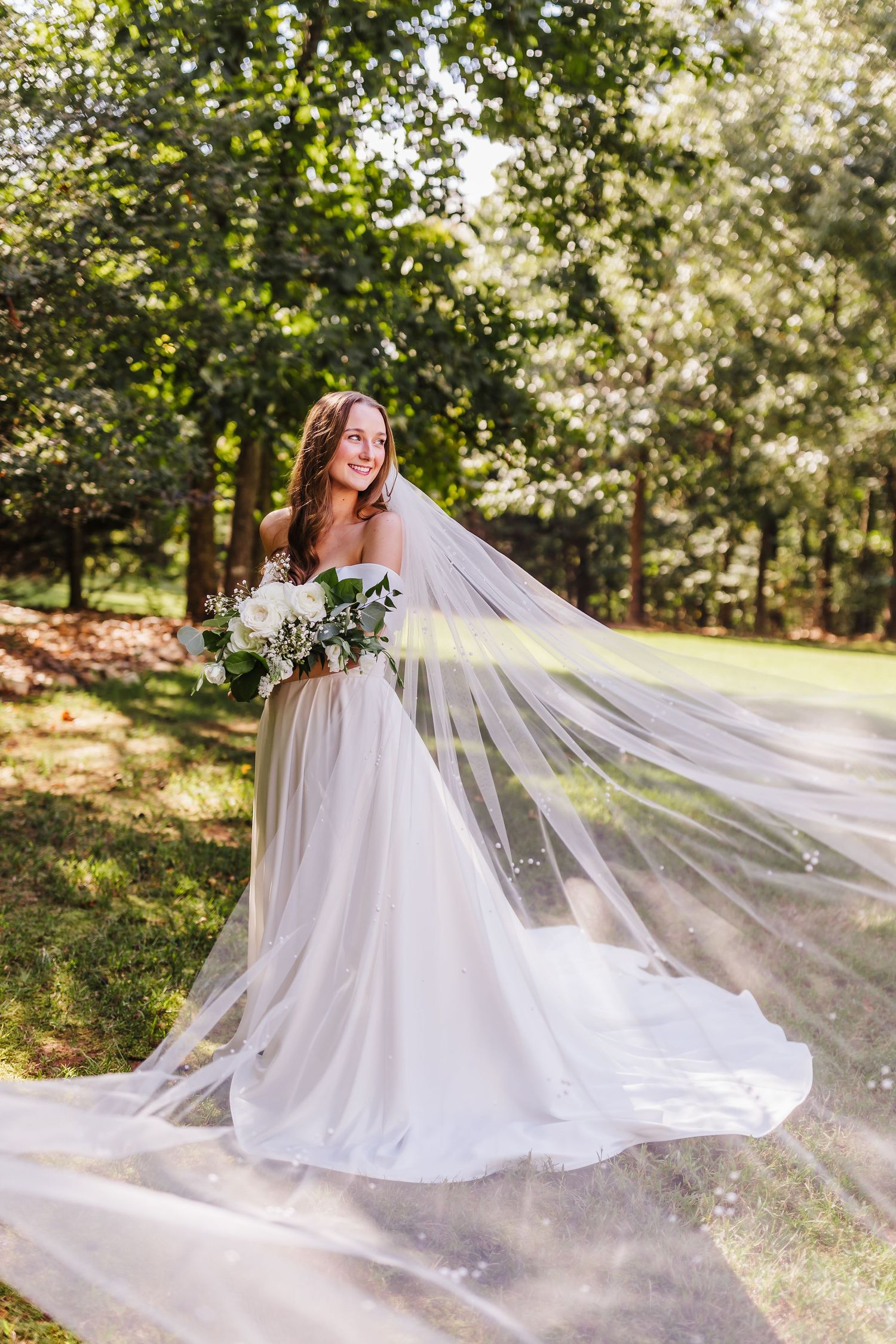 Flowing white wedding dress with long veil photographed in outdoor garden setting.