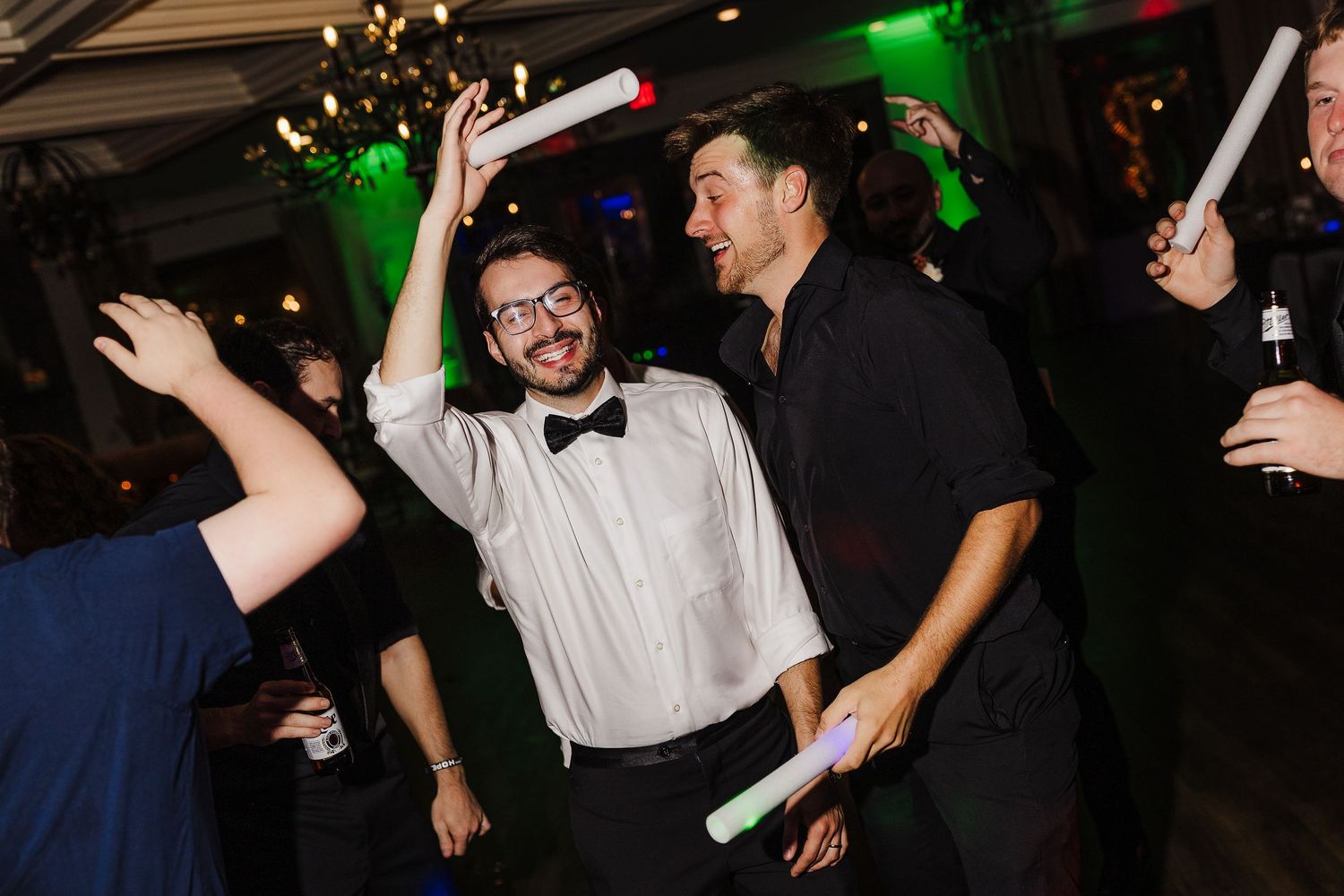 People dancing and celebrating at a dimly lit party venue with colorful lighting and festive atmosphere.