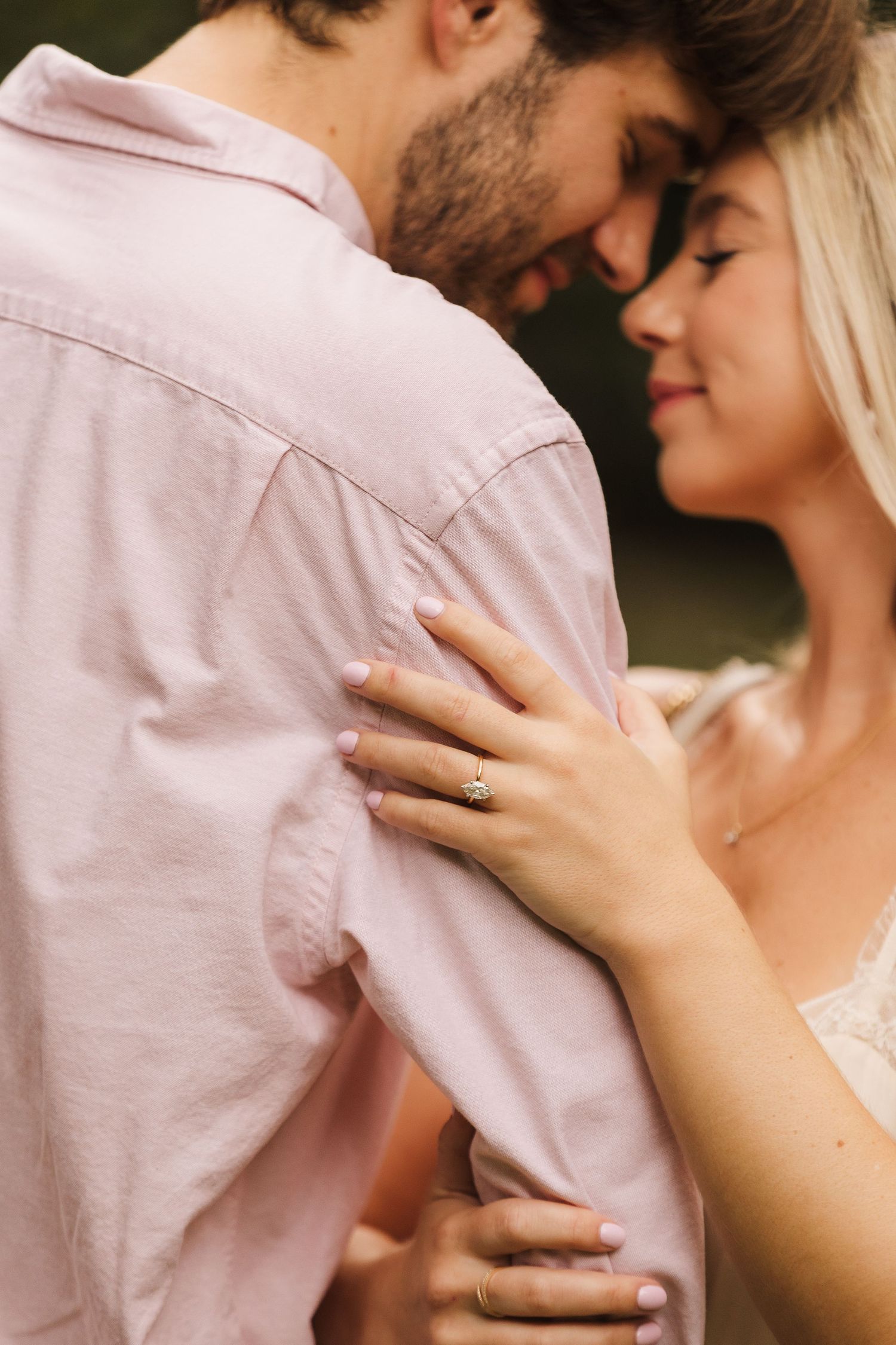 Couple sharing an intimate moment, woman wearing an engagement ring embracing man in pink shirt.