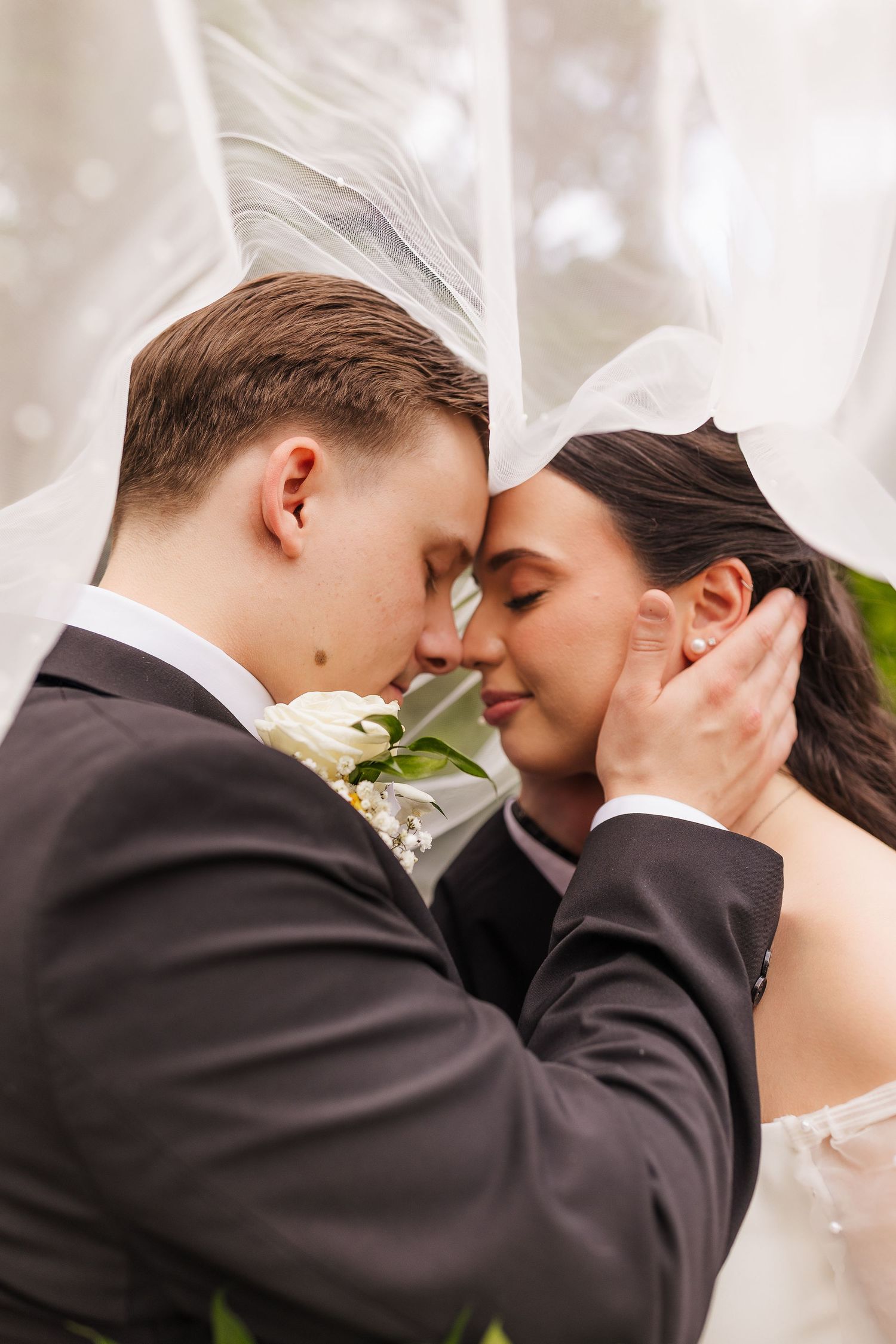 Bride and groom share a romantic forehead touch under a flowing white veil on their wedding day.