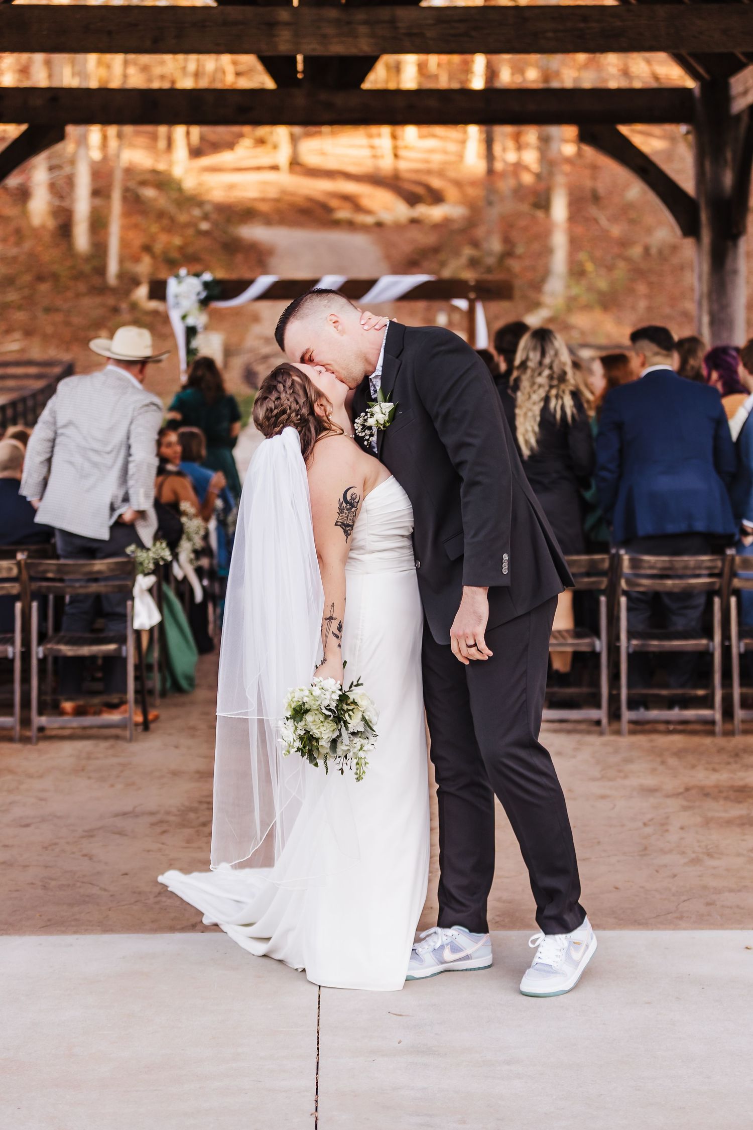 Wedding ceremony in a rustic barn venue with guests seated on wooden benches.
