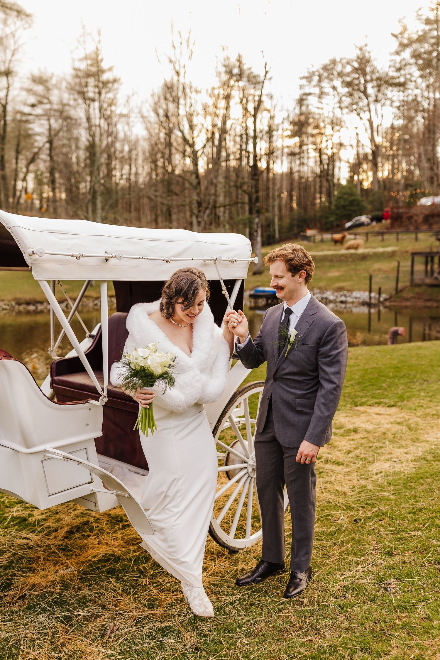 Bride stepping out of white horse-drawn carriage holding bouquet while groom assists her at outdoor wedding venue.