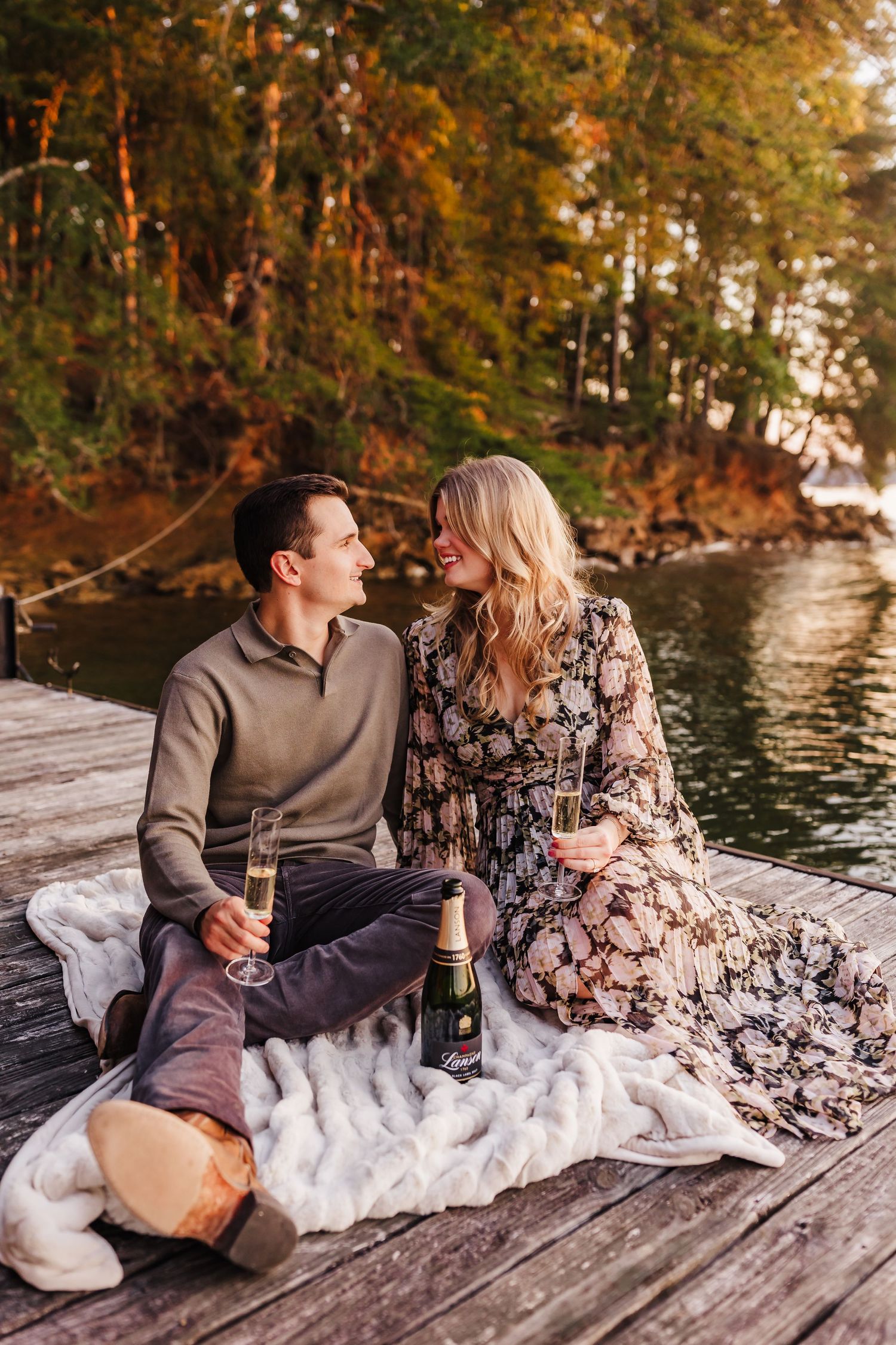 A romantic picnic on a dock by a lake with champagne and a cozy blanket during autumn.