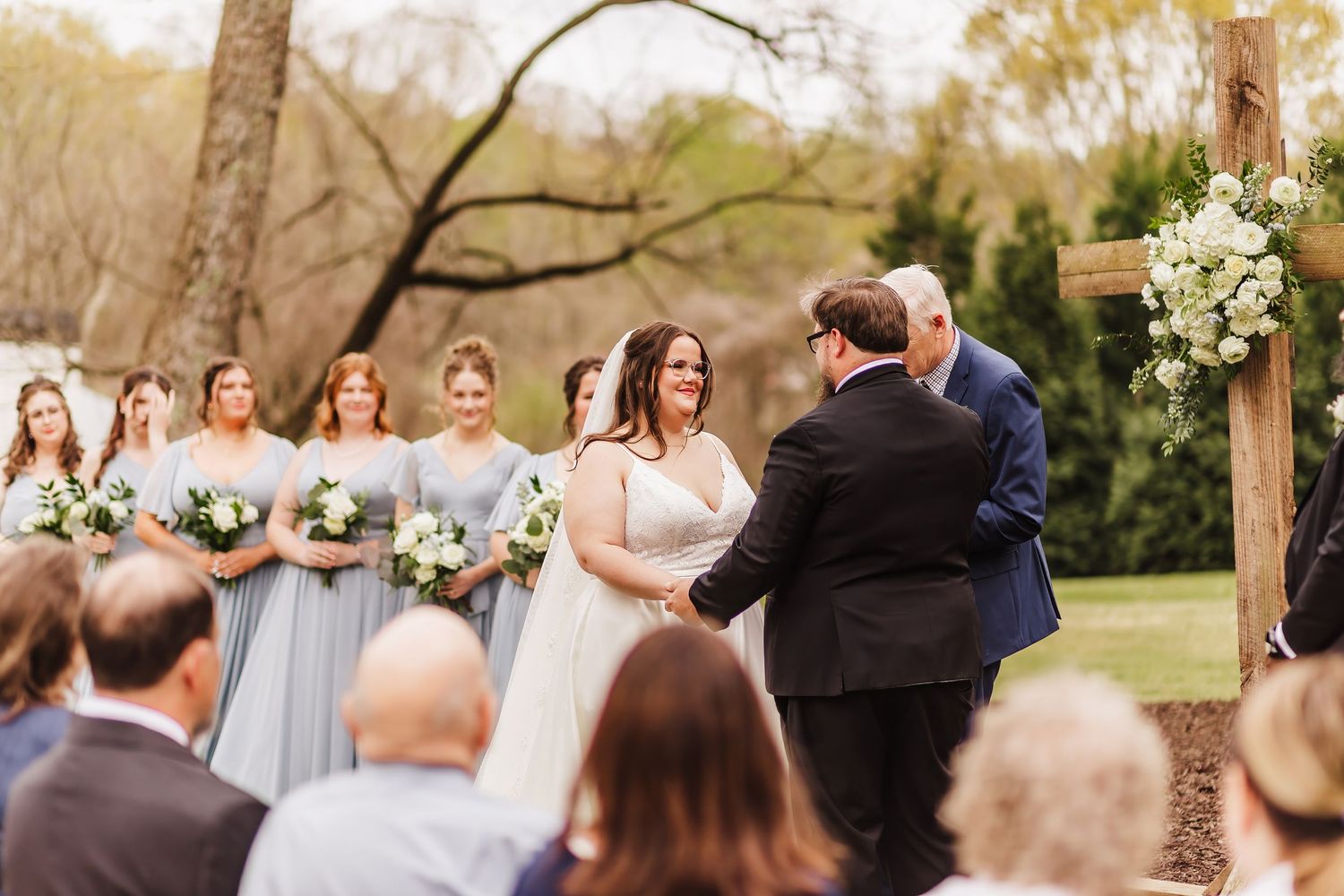 Outdoor wedding ceremony under trees at Chapman Hill with guests seated on white chairs.