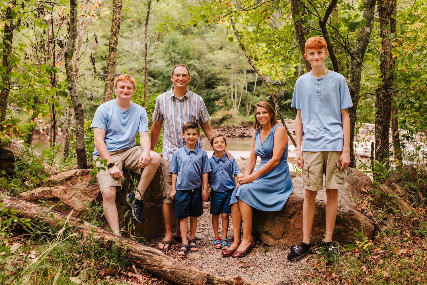 Family sitting together on large tree roots in forested setting during outdoor photo session.