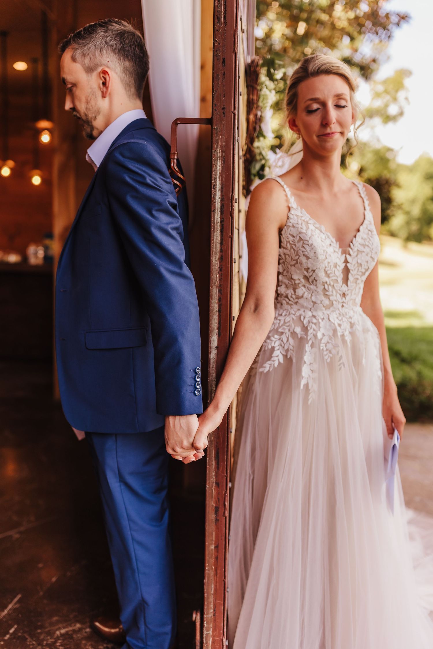 Bride and groom sharing a first touch moment from opposite sides of a doorway before the ceremony at Walters Barn with natural light.