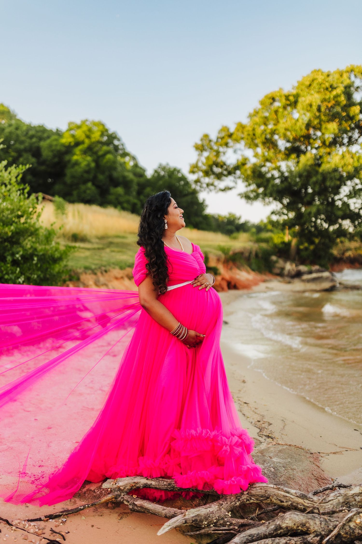 Outdoor maternity portrait at Vann’s Tavern Park featuring an expecting mother in a flowing pink gown by the water.