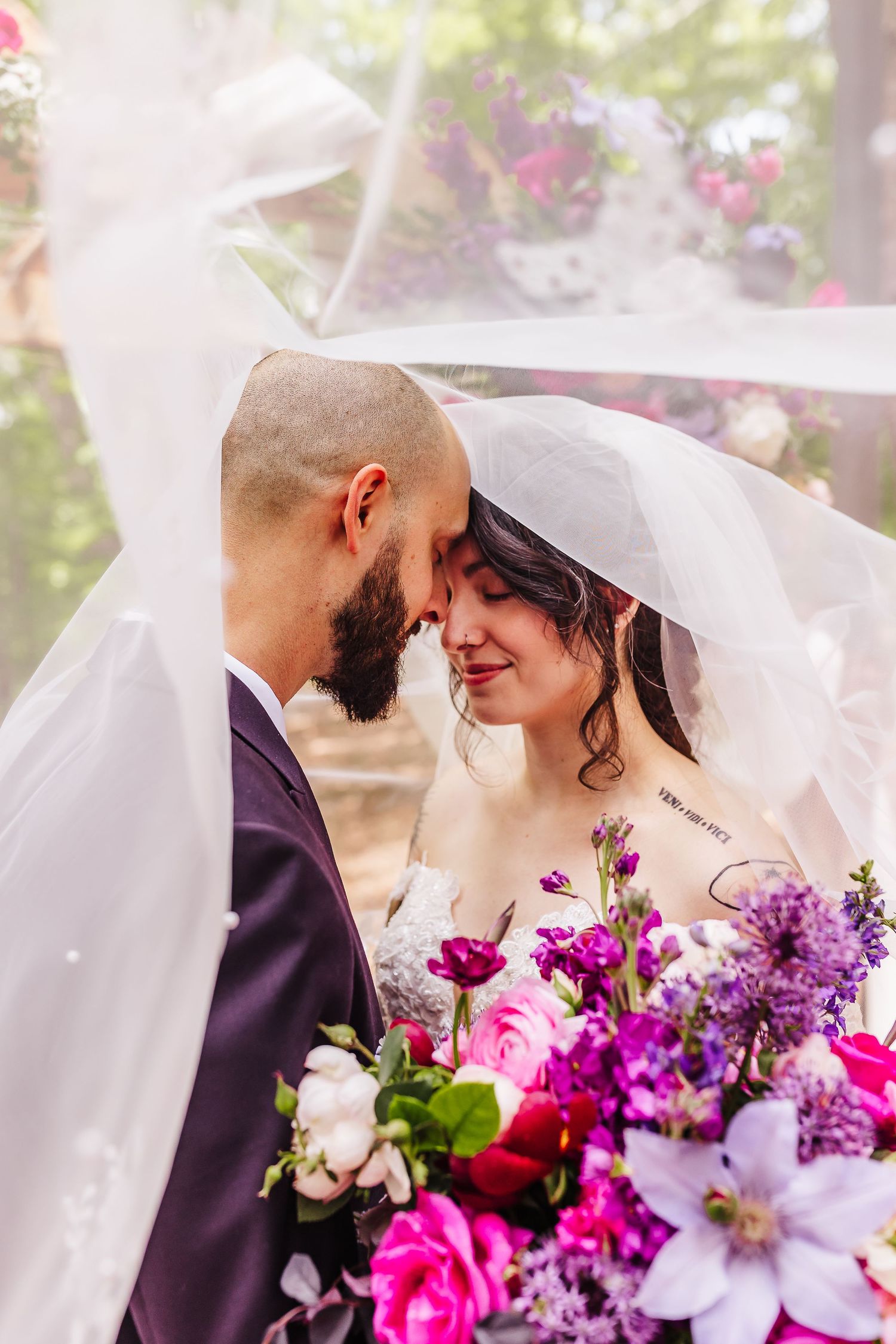 Romantic moment under veil with vibrant pink and purple floral bouquet.