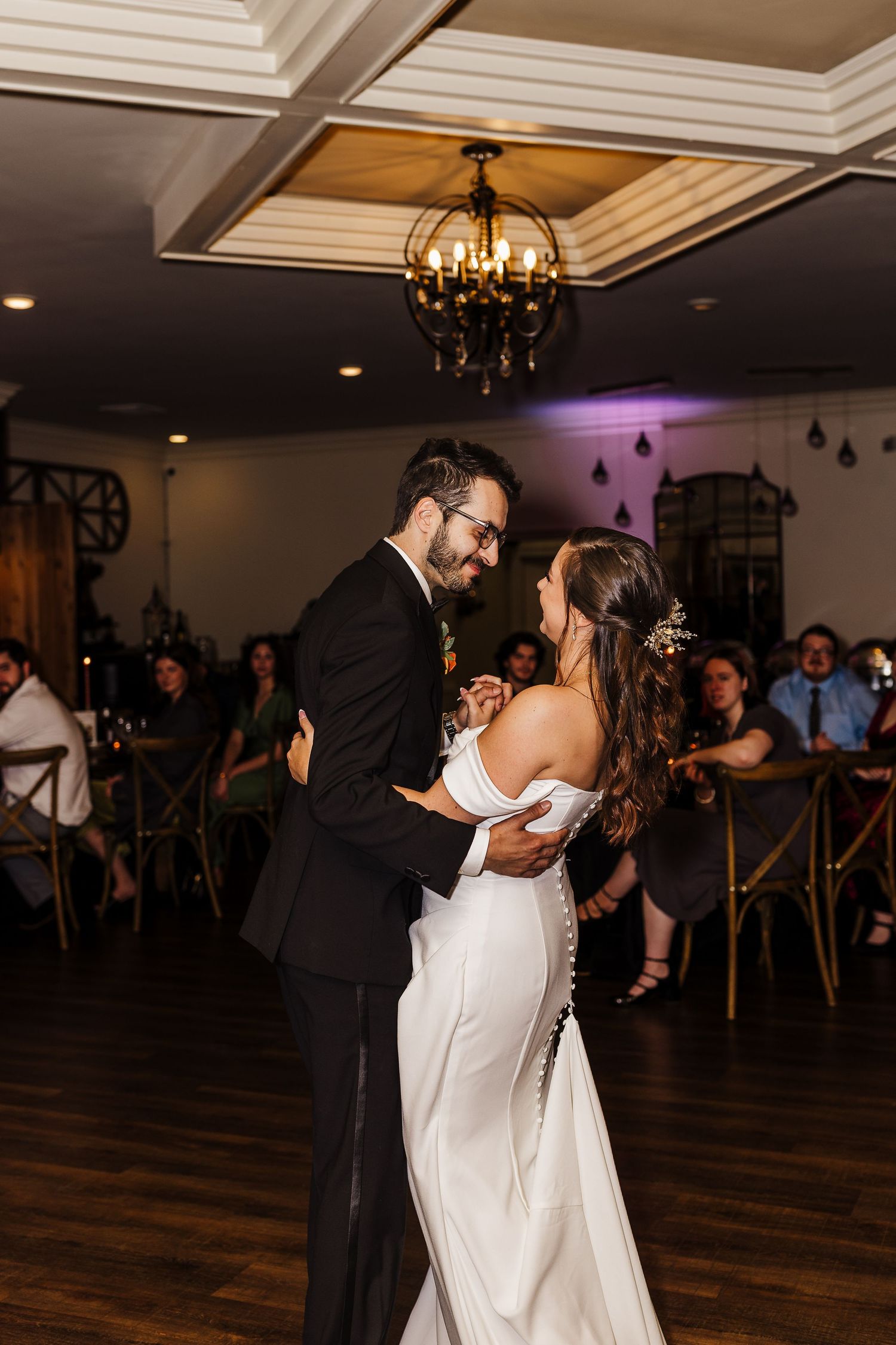 Newlyweds share a romantic dance together during their wedding reception on a dark wooden dance floor.