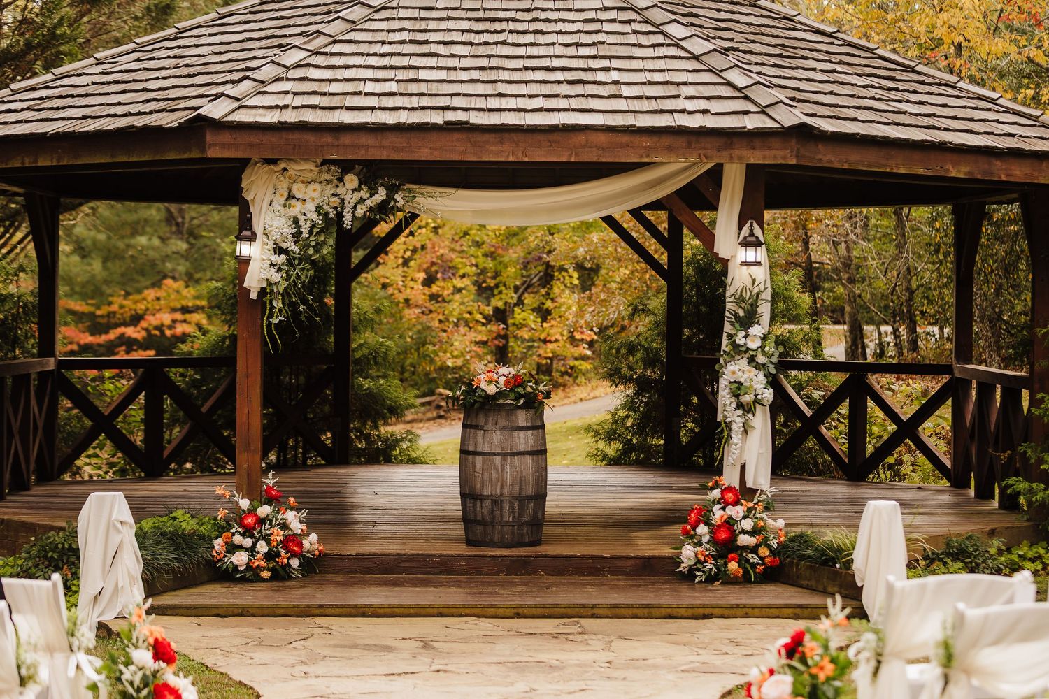 A rustic wooden gazebo decorated with flowers and wine barrel for an outdoor wedding ceremony in autumn.