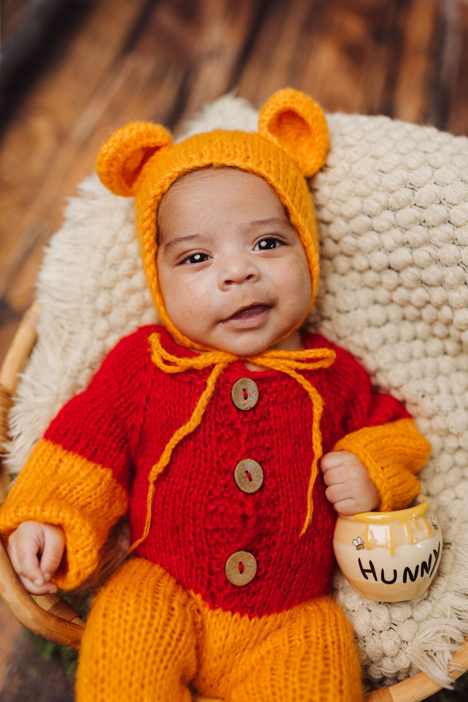 A photo showing a baby wearing an orange and red knitted story book inspired outfit with ears and buttons.