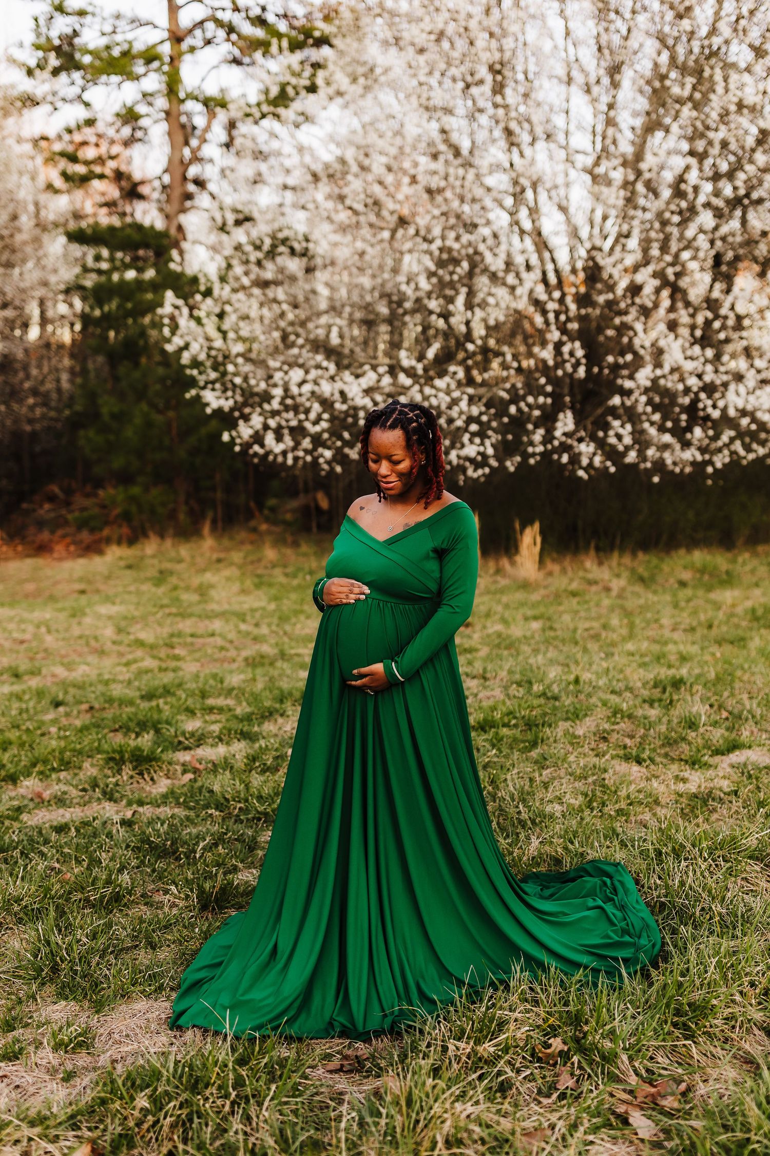 Expecting mother holding her belly and looking down during a spring maternity session at Little Mulberry Park, wearing an emerald green dres