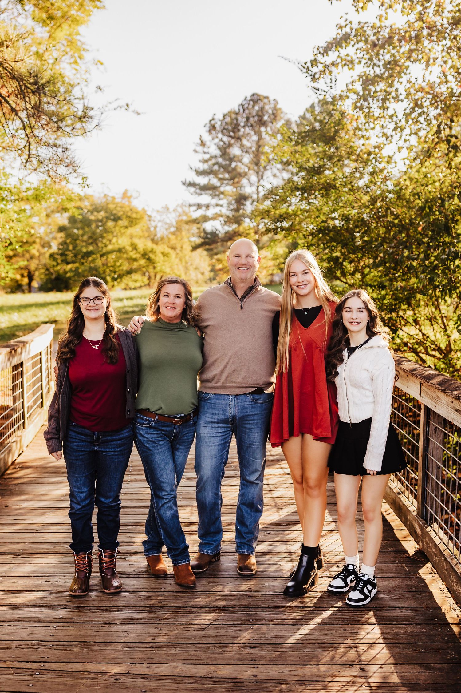 Family of five posing together on wooden bridge during fall season portrait session.
