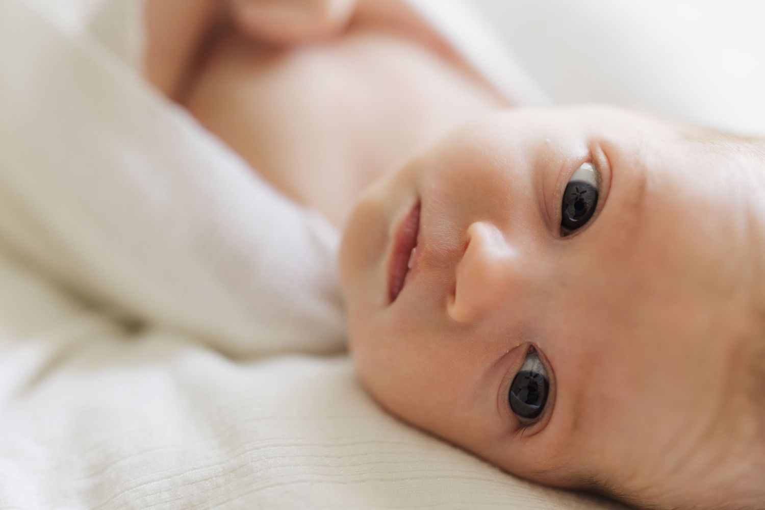 Close up portrait of a baby lying down with wide eyes looking directly at camera.