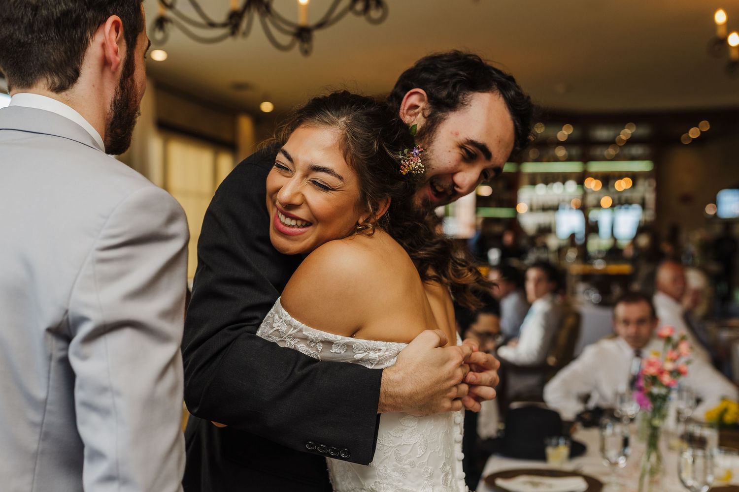 Joyful bride receives a warm hug from a guest during wedding reception celebration indoors.
