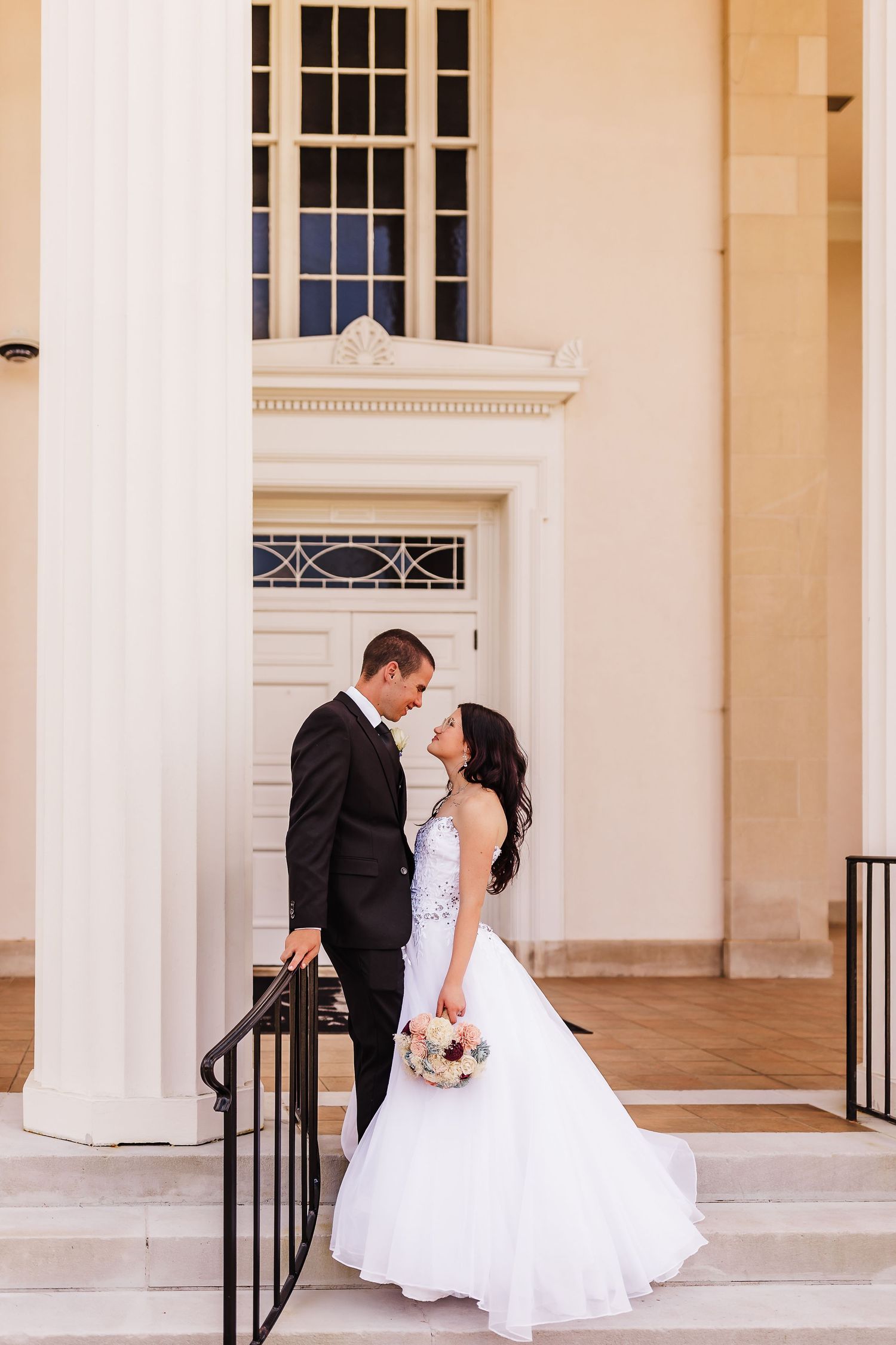 Elegant wedding portrait on classic white columned entrance with black railings.