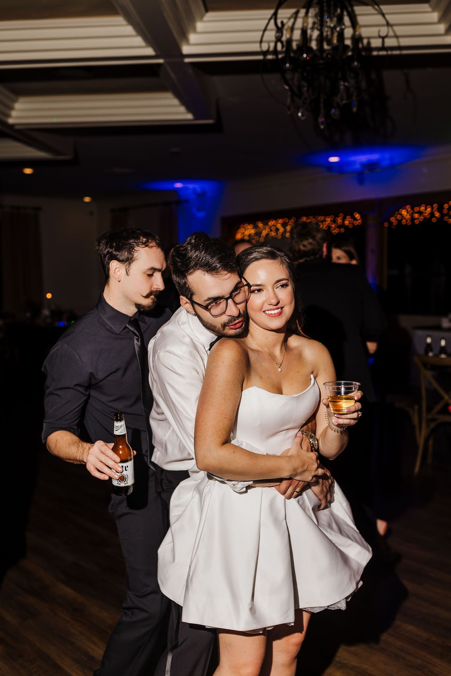 Wedding guests dancing and celebrating together at a dimly lit reception venue with blue lighting.