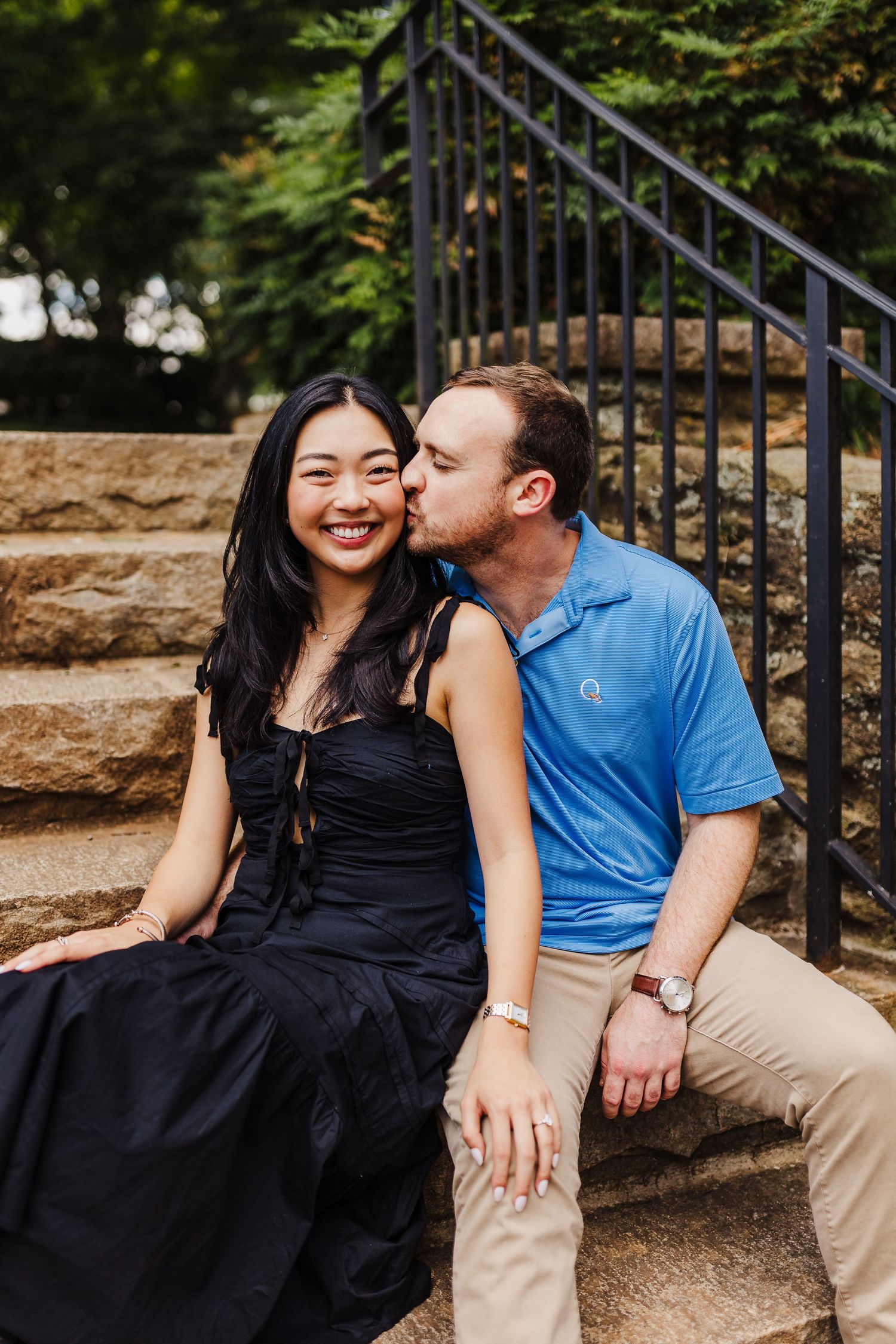 A couple sitting together on stone steps with black railings.