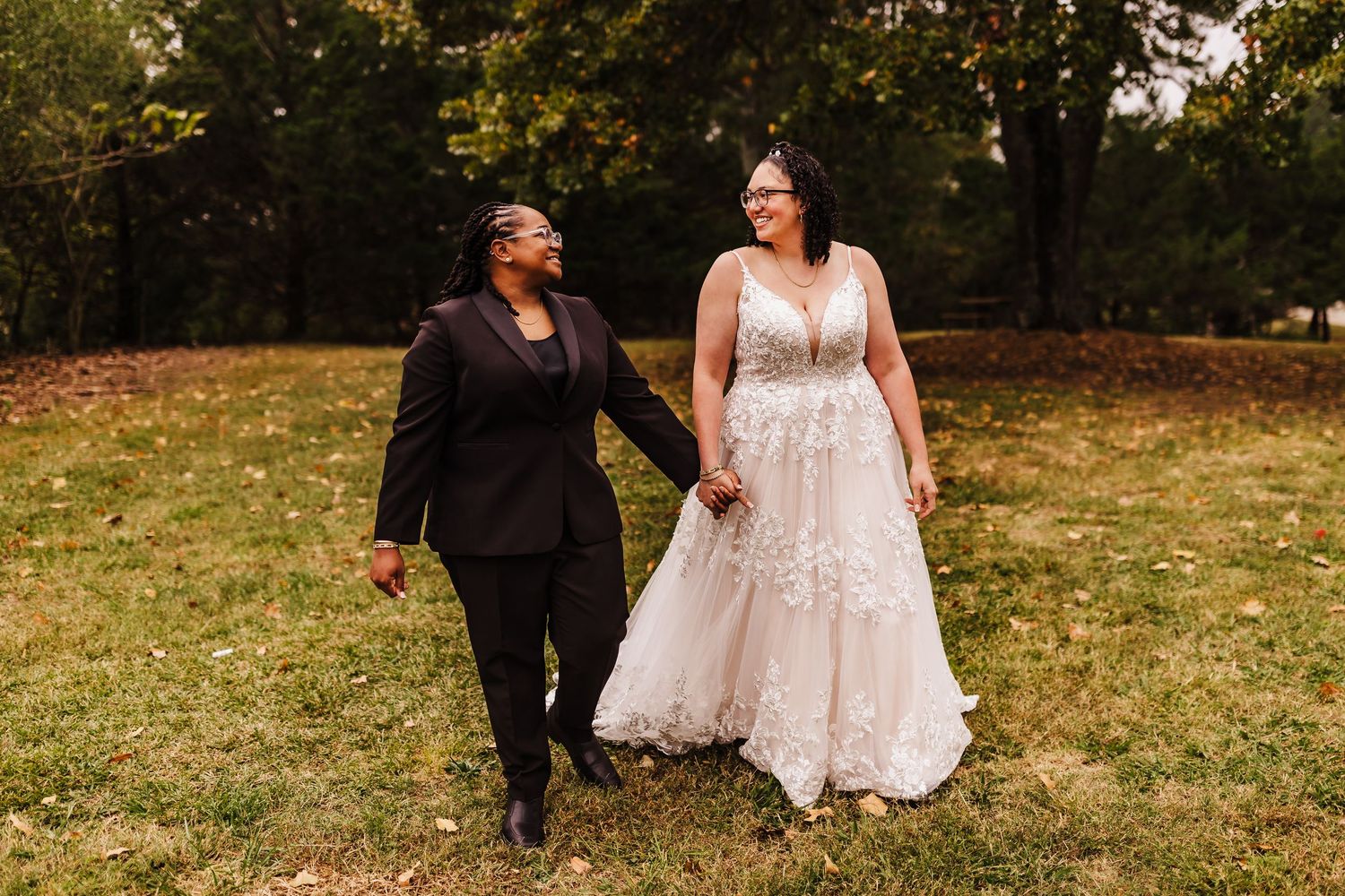 Two people walking and laughing together on autumn grass during wedding celebration.