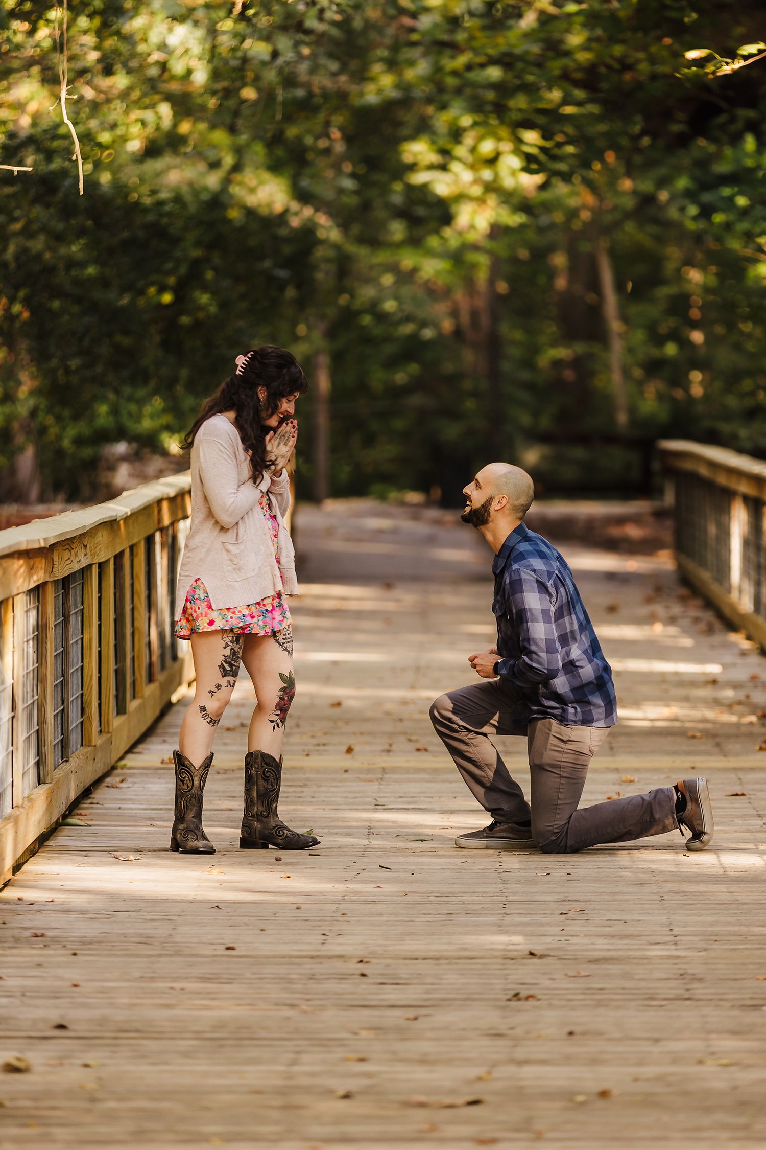 A candid proposal moment captured on a wooden bridge walkway surrounded by autumn foliage.