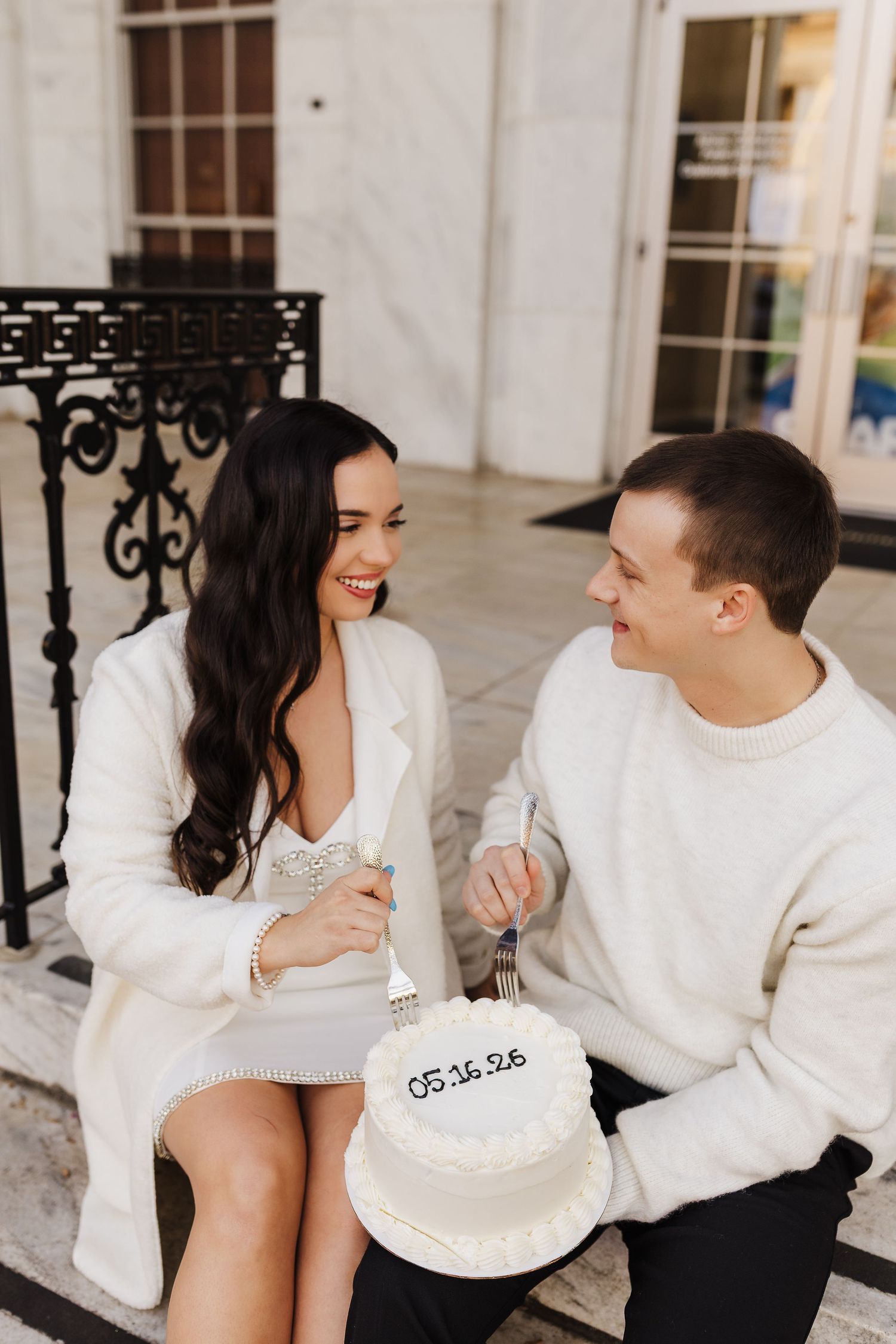 Engaged couple smiling together while sharing a cake during an engagement session in Athens.